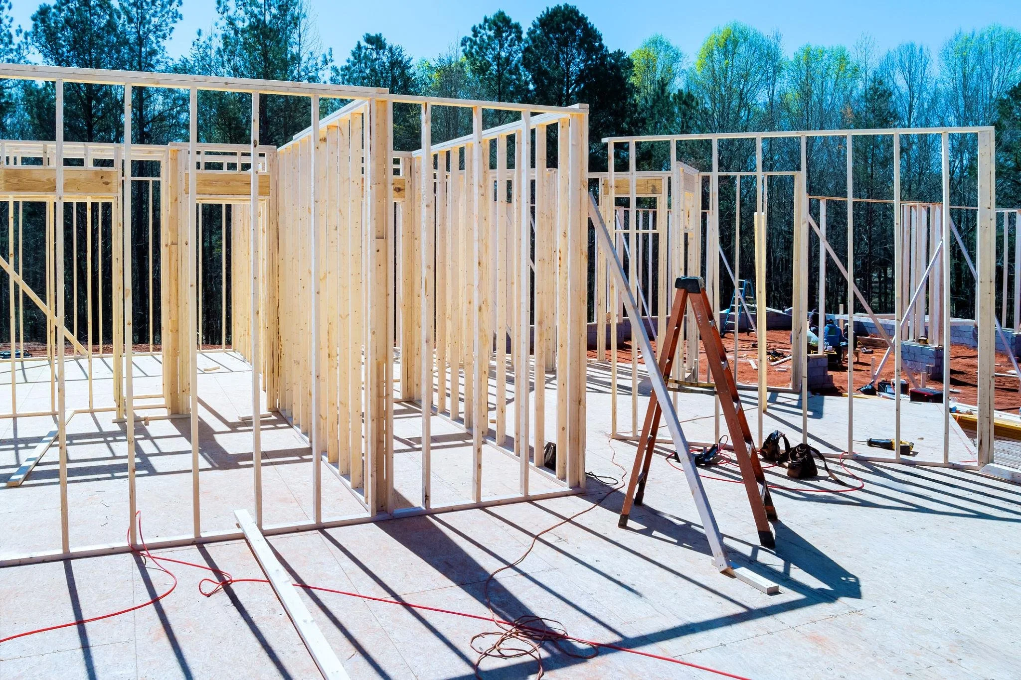 Wooden framing in the early stages of house construction on an outdoor site with trees in the background.