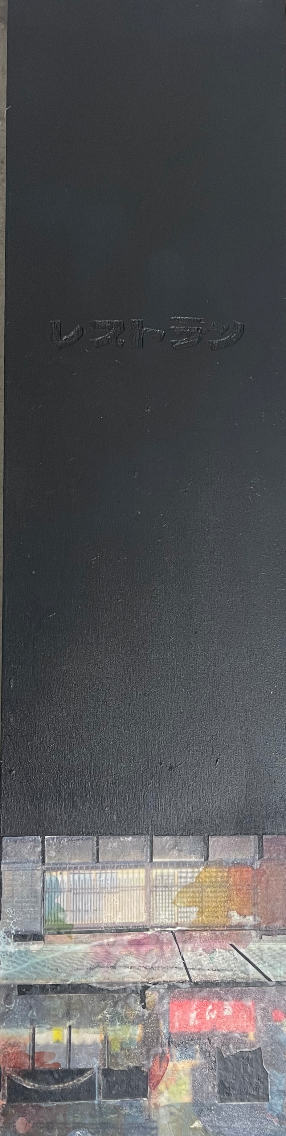 Tall black menu or signboard with Japanese text engraved on it, and a blurred colorful street scene at the bottom