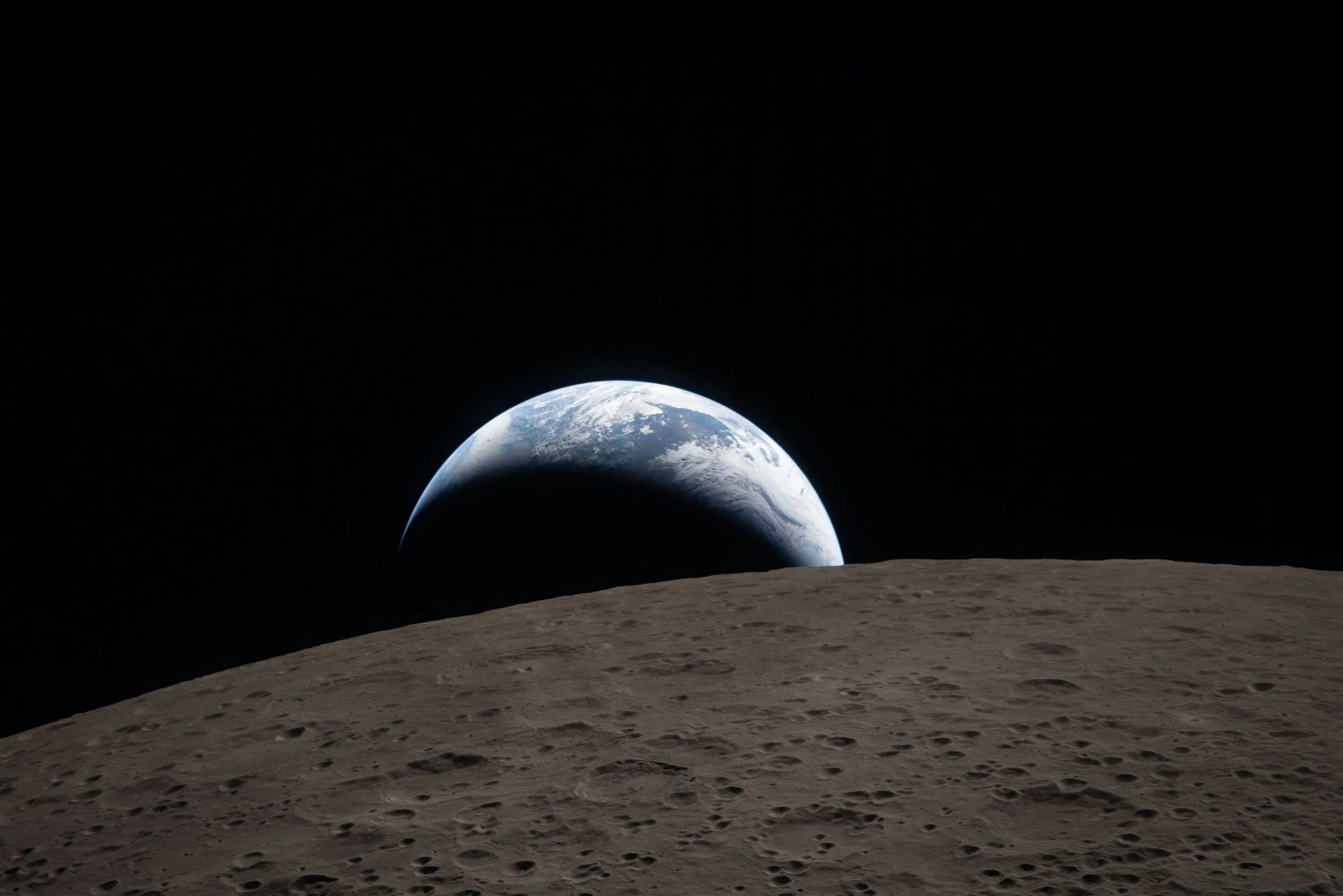 View of Earth from the moon's surface with a cratered moon landscape in the foreground.