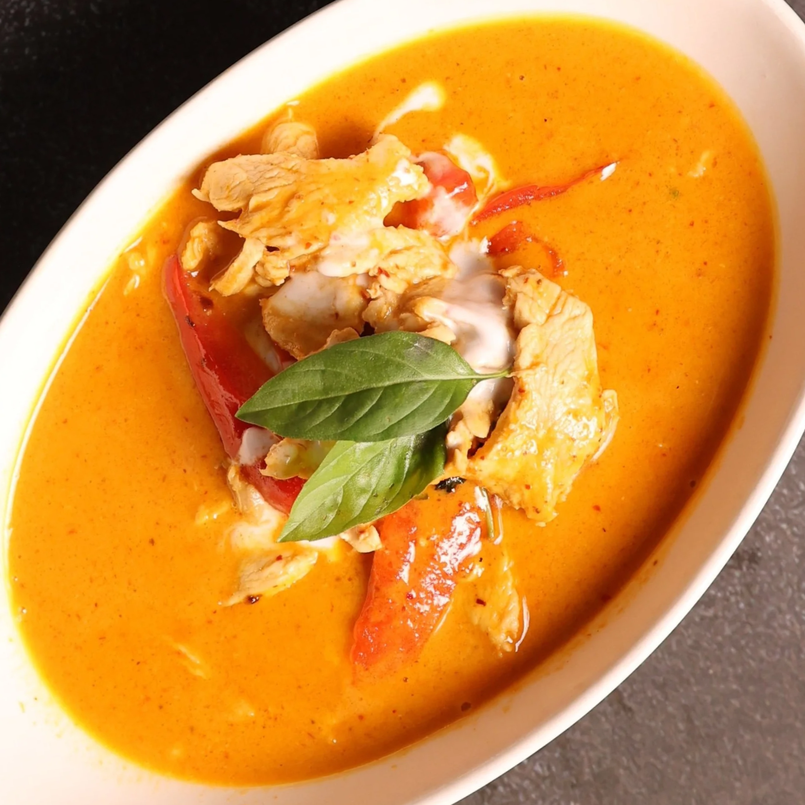 Bowl of Thai red curry with chicken, red bell peppers, and basil leaves.