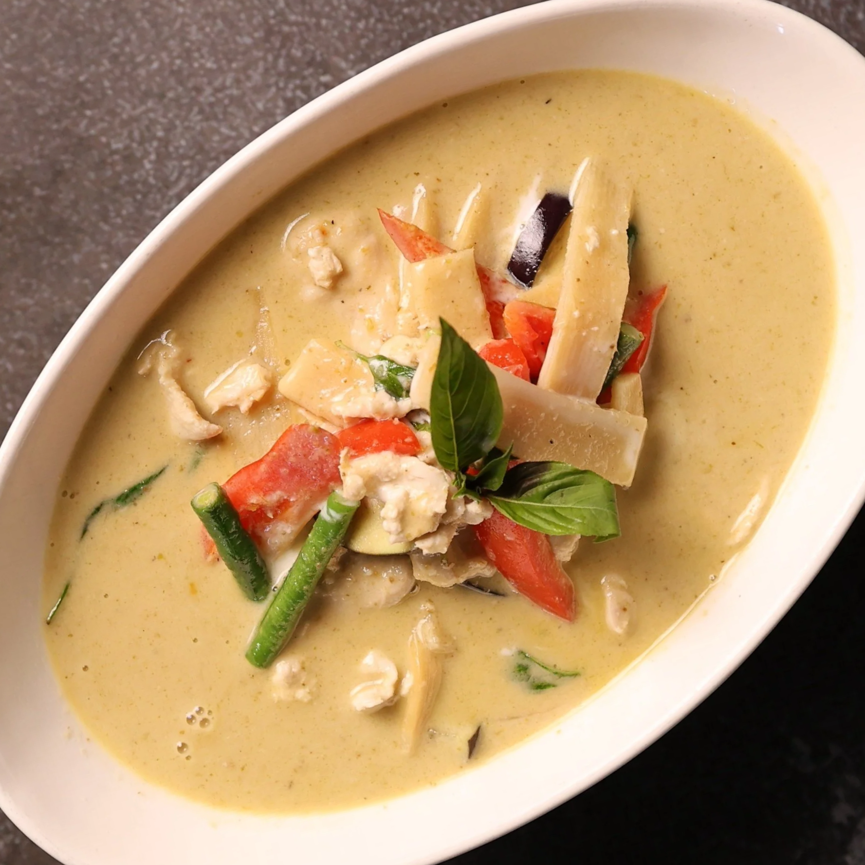 Bowl of creamy vegetable soup garnished with red peppers, eggplant, green beans, basil, and cheese.