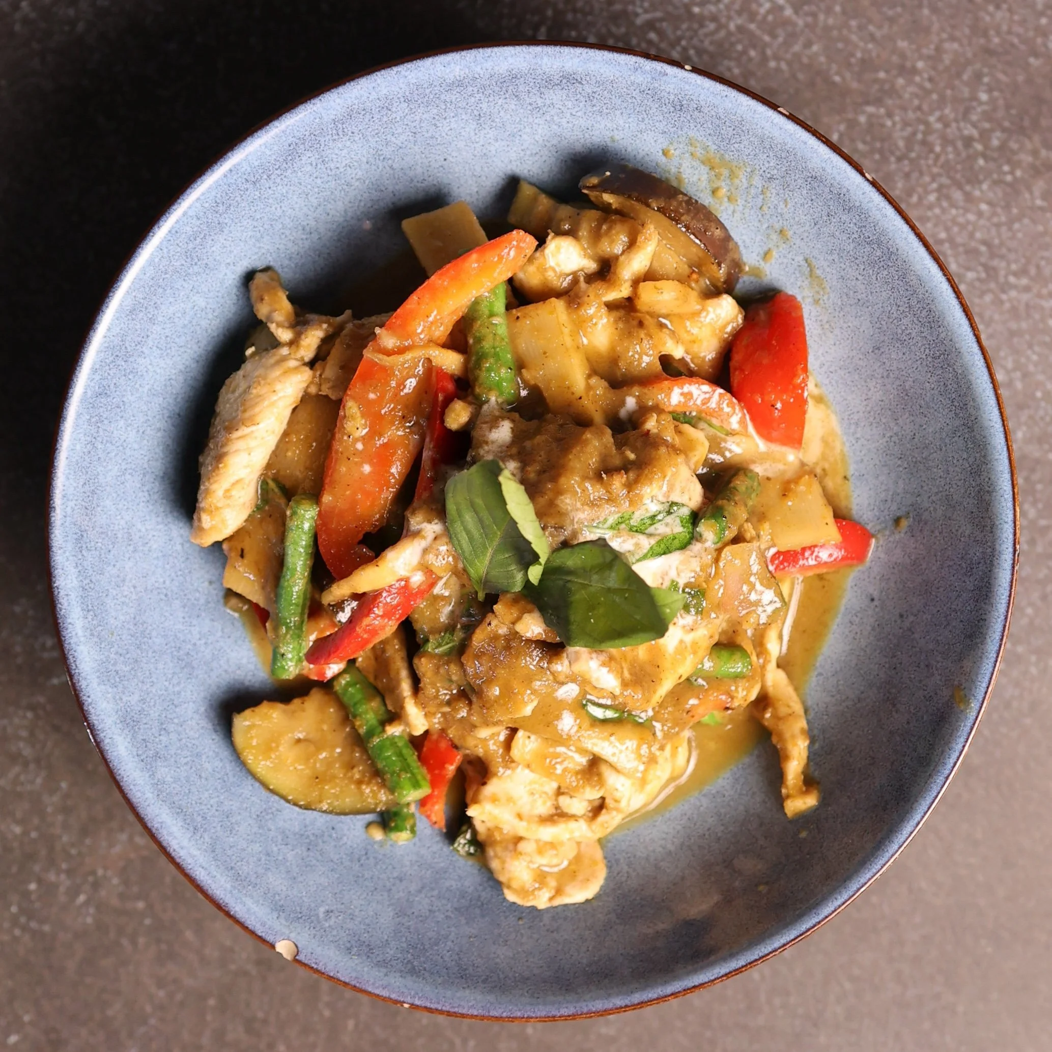 A bowl of stir-fried vegetables and chicken with red and green peppers, eggplant, and zucchini in a yellow sauce.