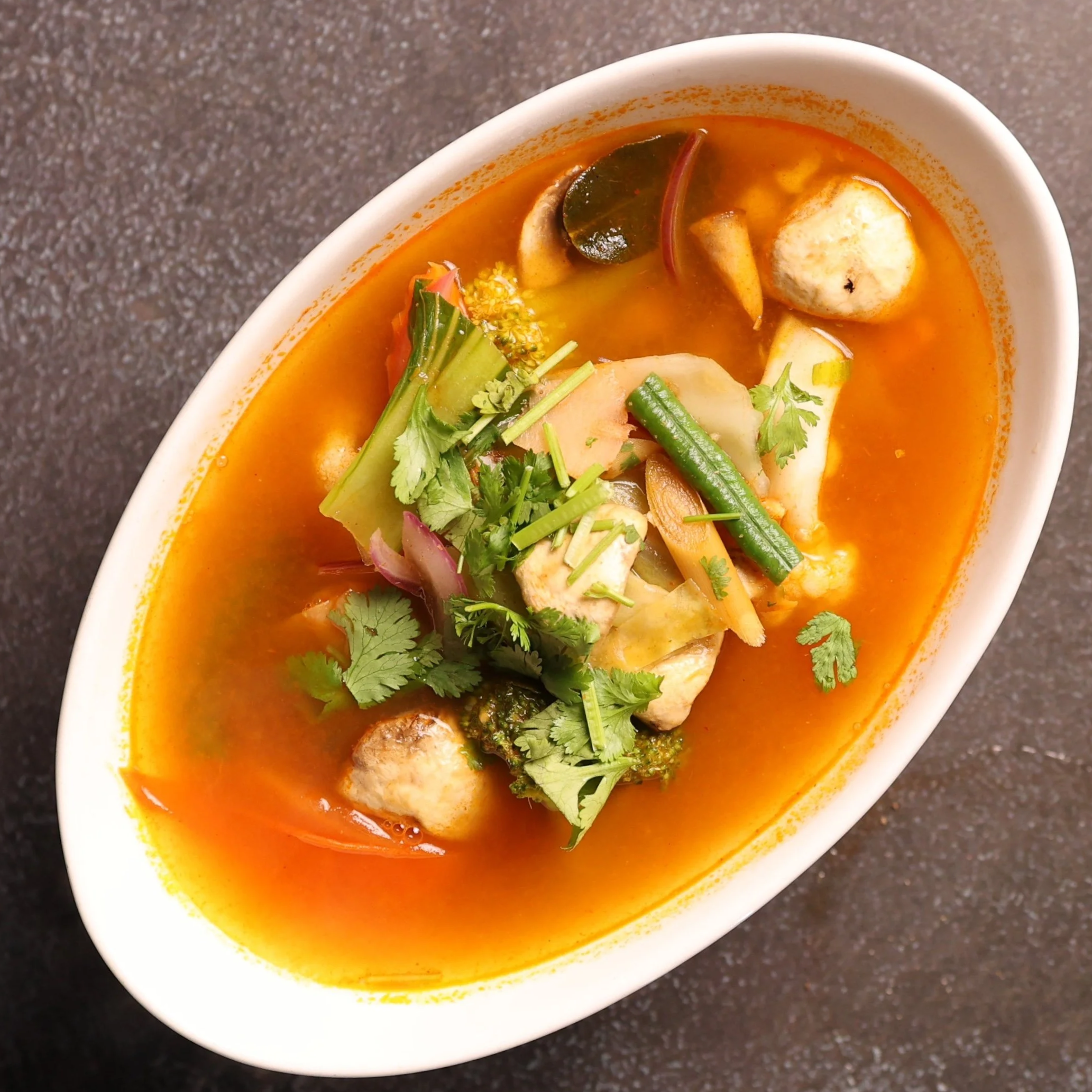 Bowl of vibrant orange curry with visible vegetables and herbs.