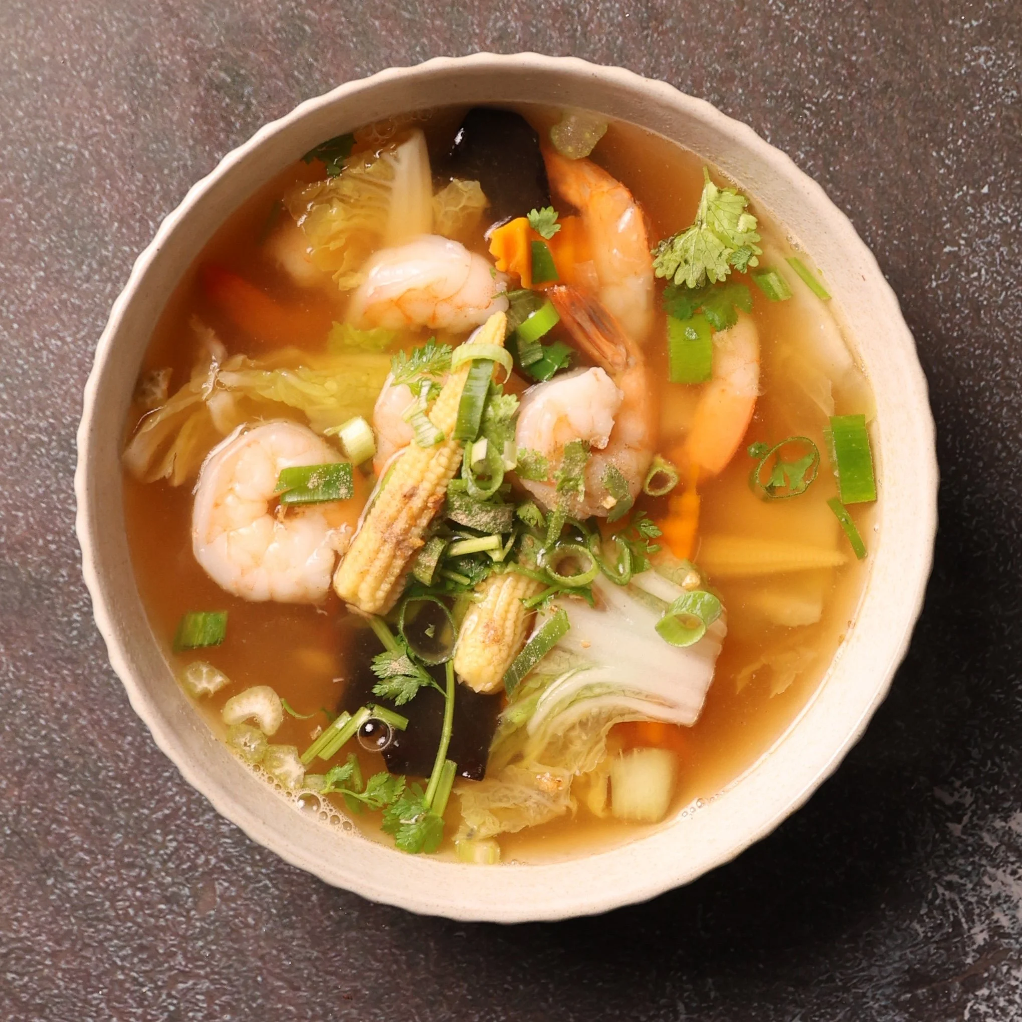 A bowl of seafood soup with shrimp, vegetables, and herbs.