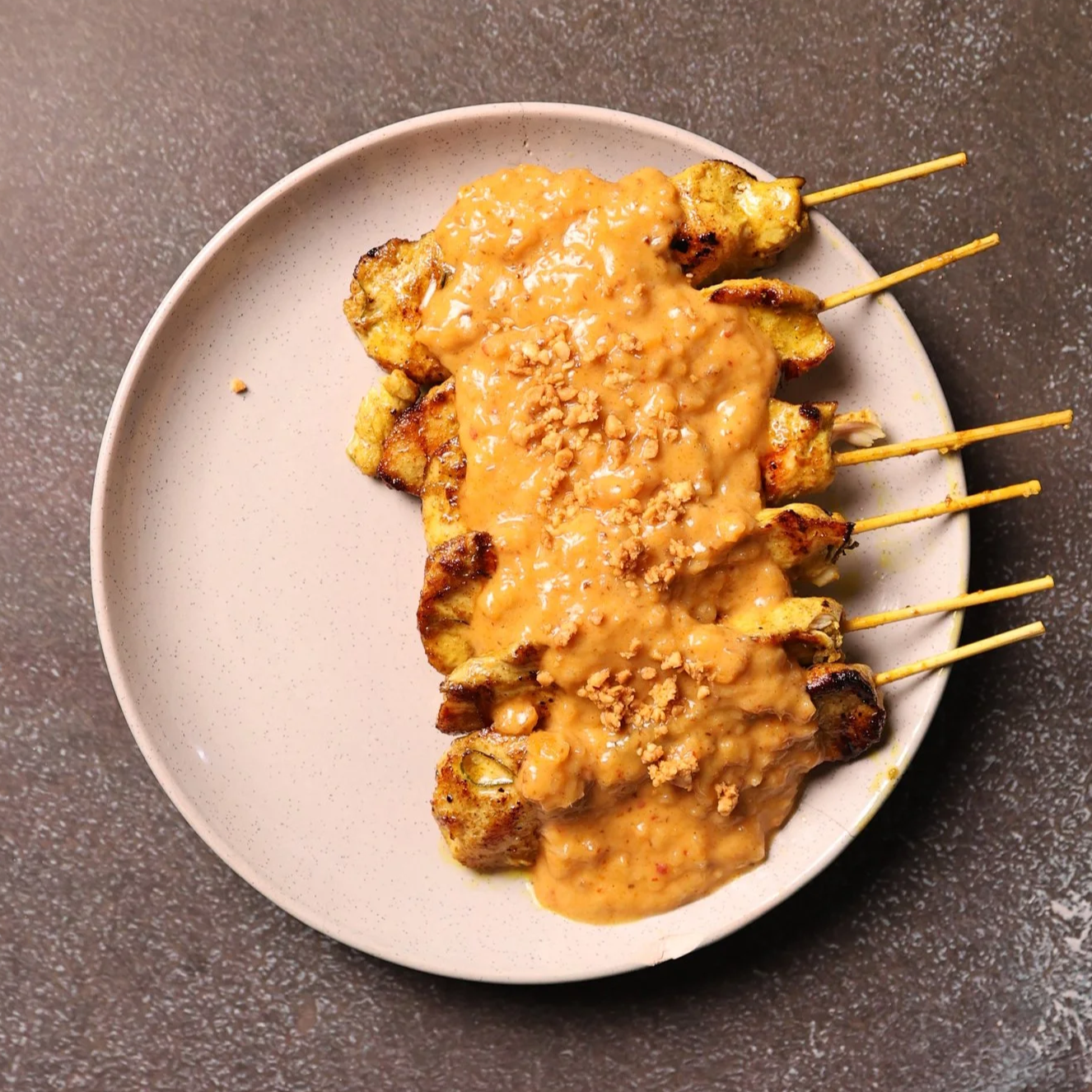 Plate of grilled chicken satay skewers topped with a peanut sauce and chopped peanuts.