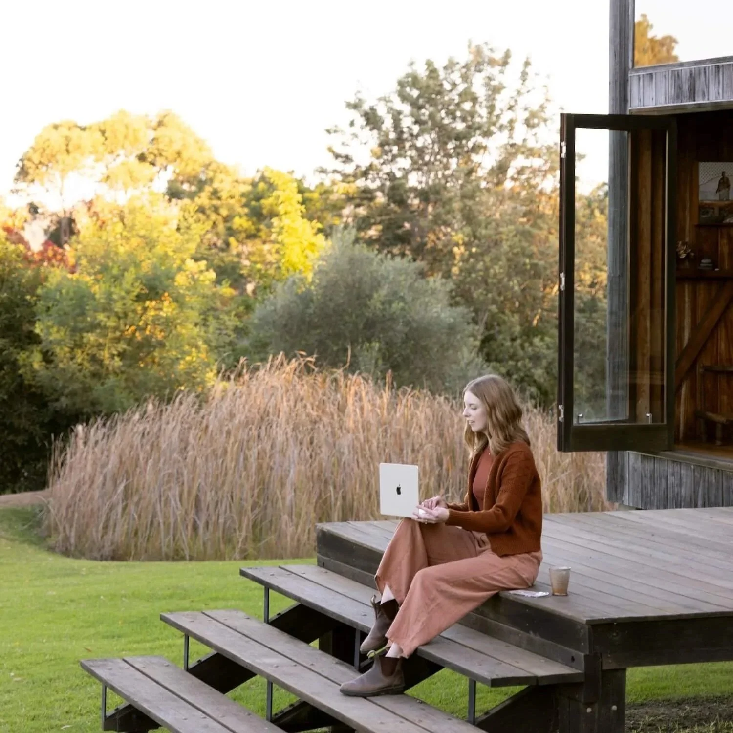 Bea Bobbin sitting on outdoor steps with a laptop, surrounded by light and open natural landscape