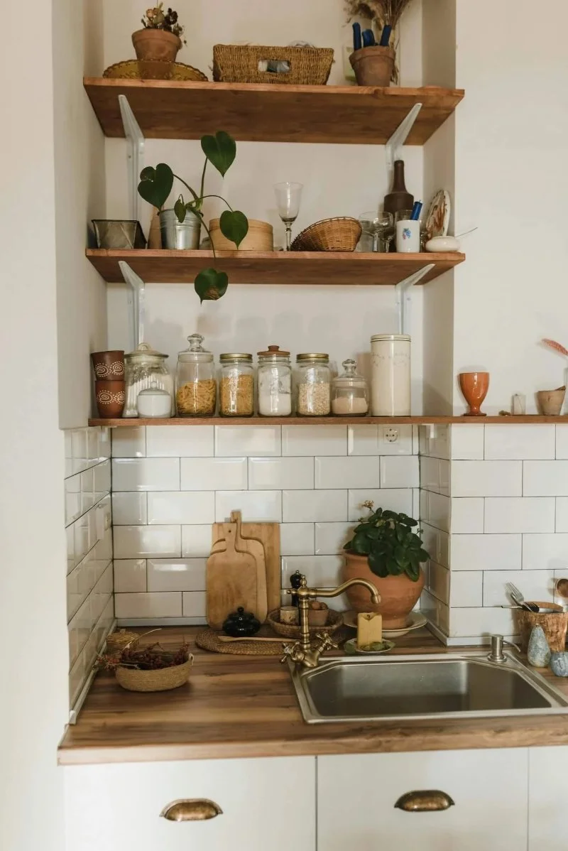 Open wooden kitchen shelves with glass jars of pasta, rice and flour above white subway tiles, a simple idea for how to organize a pantry