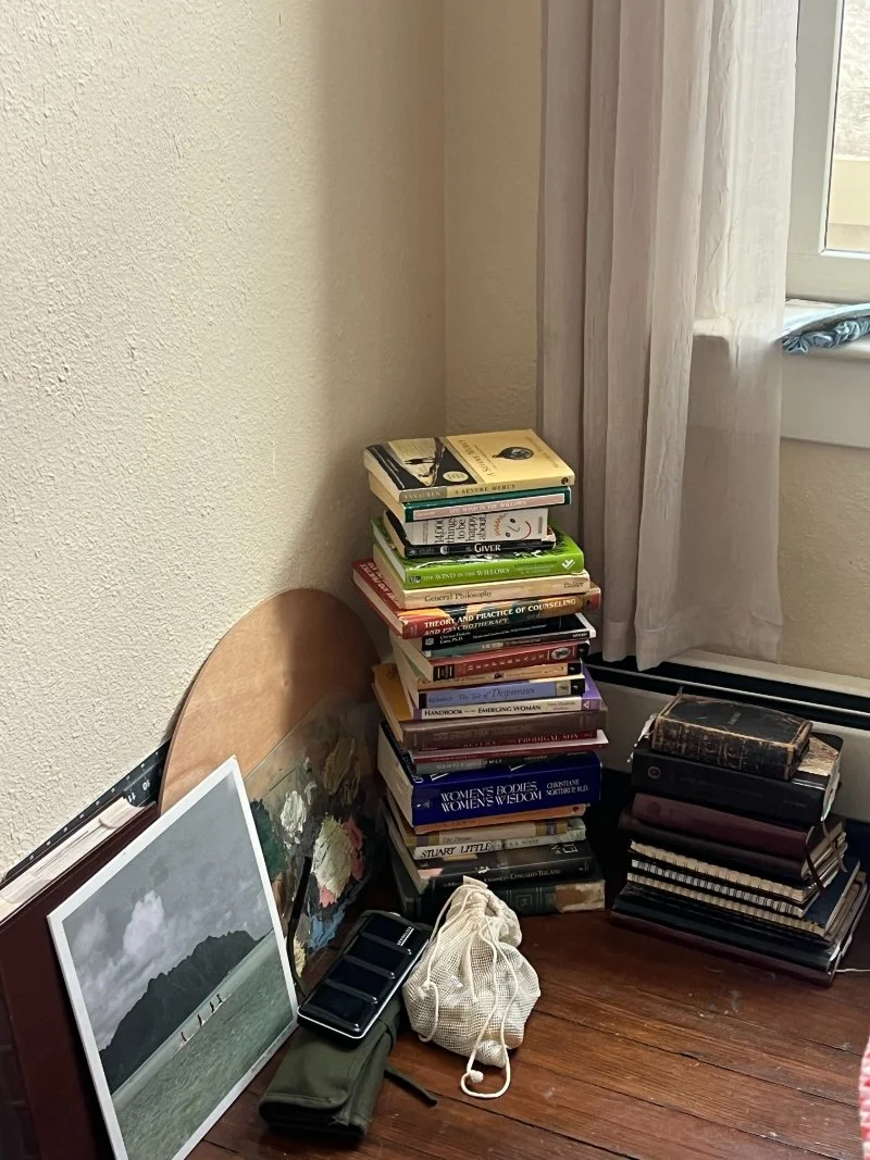 Stacked piles of books, art supplies and a framed print in a corner, waiting for someone to find where to donate in Canberra.