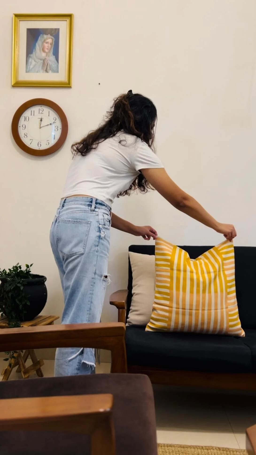 Woman straightening a yellow striped cushion on a sofa during a home tidying session