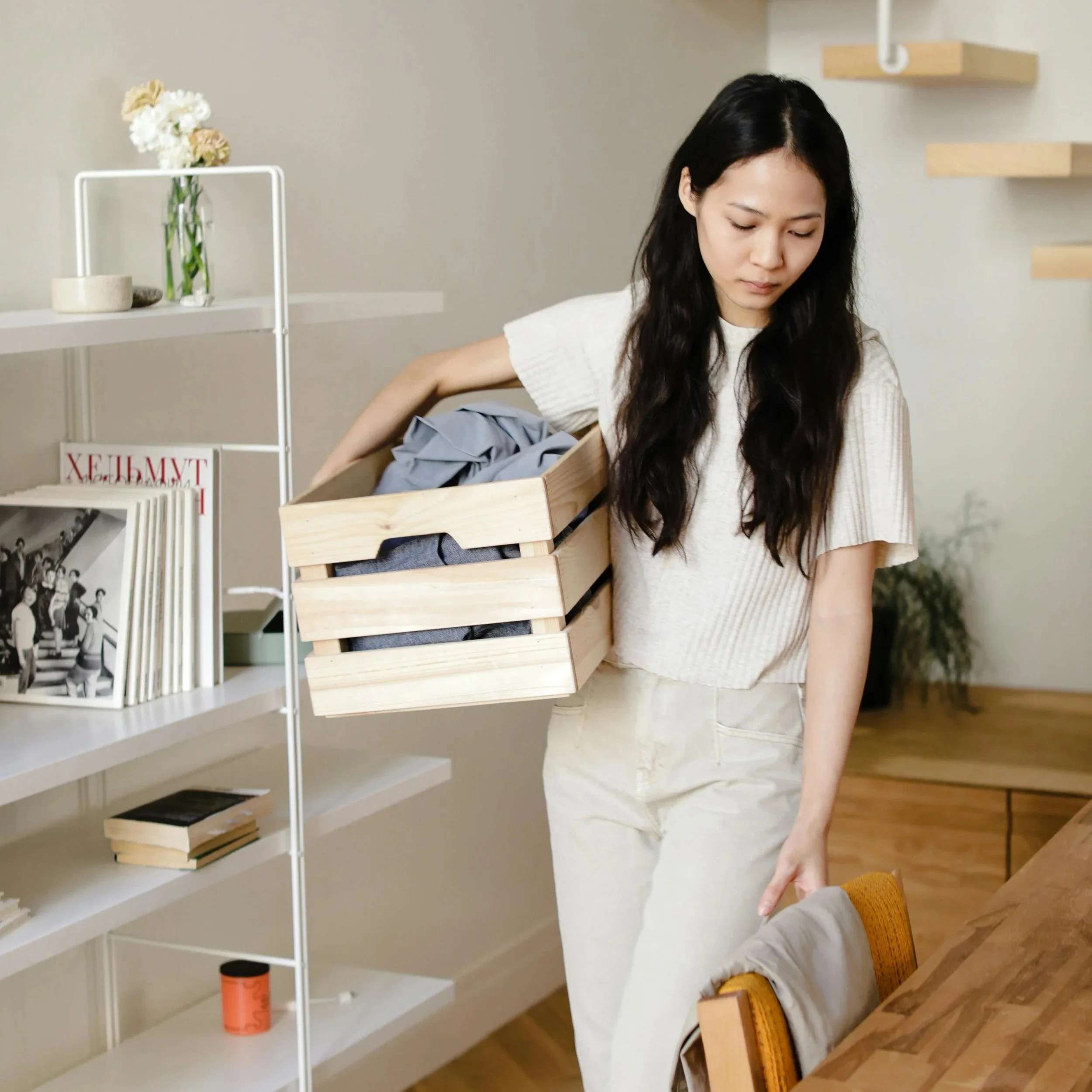 Woman with long black hair and fair skin is decluttering clothing and carrying a crate, for Hello Space Online Decluttering Coach