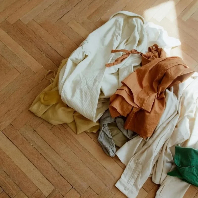 Pile of cream, mustard, rust and green clothes on a herringbone timber floor, showing why is it so hard to clean with ADHD