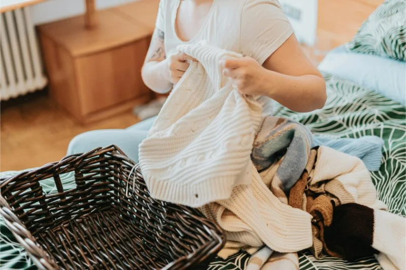 Woman holding a cream knit jumper beside a wicker basket, asking is clutter a sign of ADHD