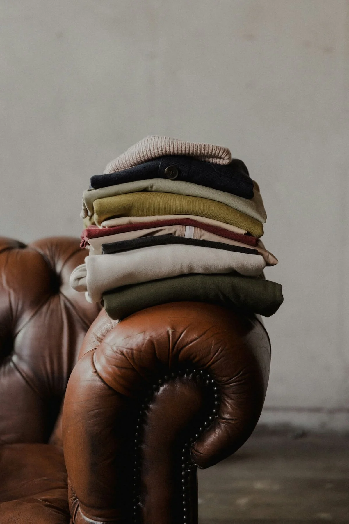 A neatly folded stack of clothing reseting on the arch of a couch