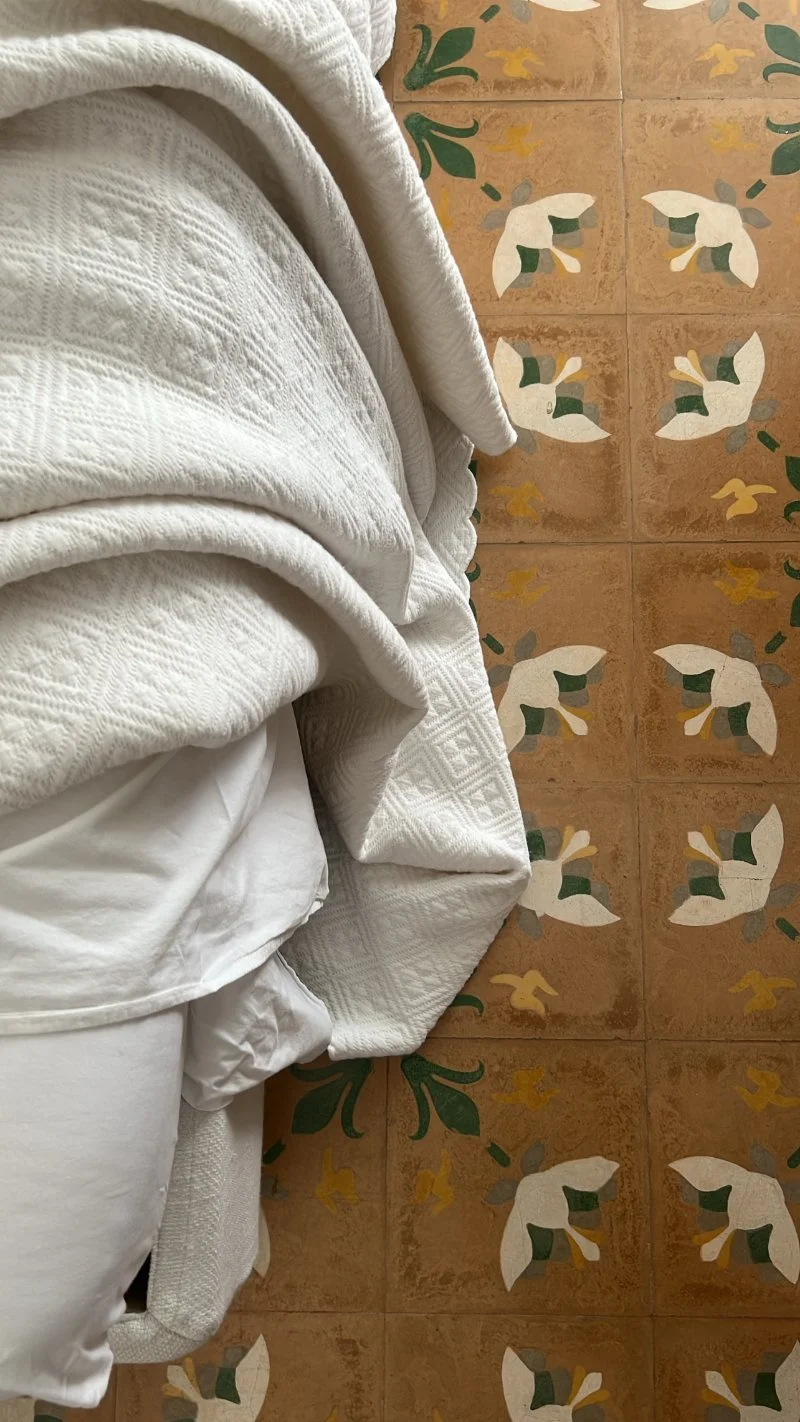 Rumpled white textured bedspread lying on a floor of patterned terracotta tiles with green and cream flowers