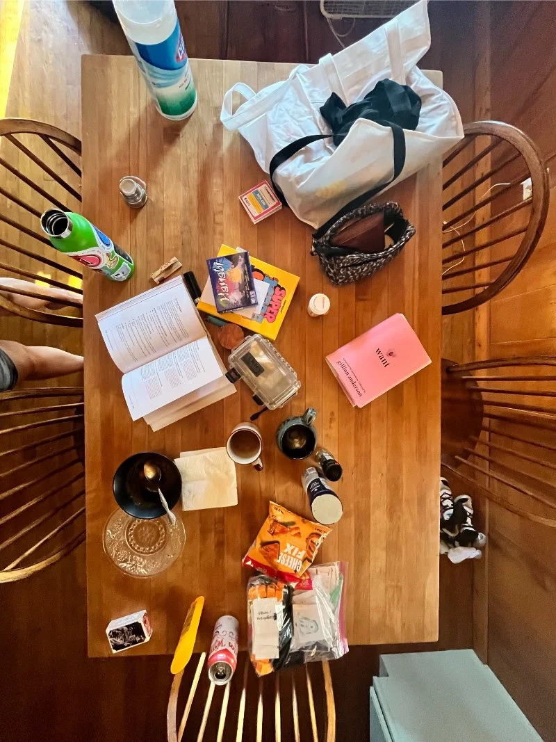 Cluttered dining table covered in bags, books and mugs, showing why my house is always messy
