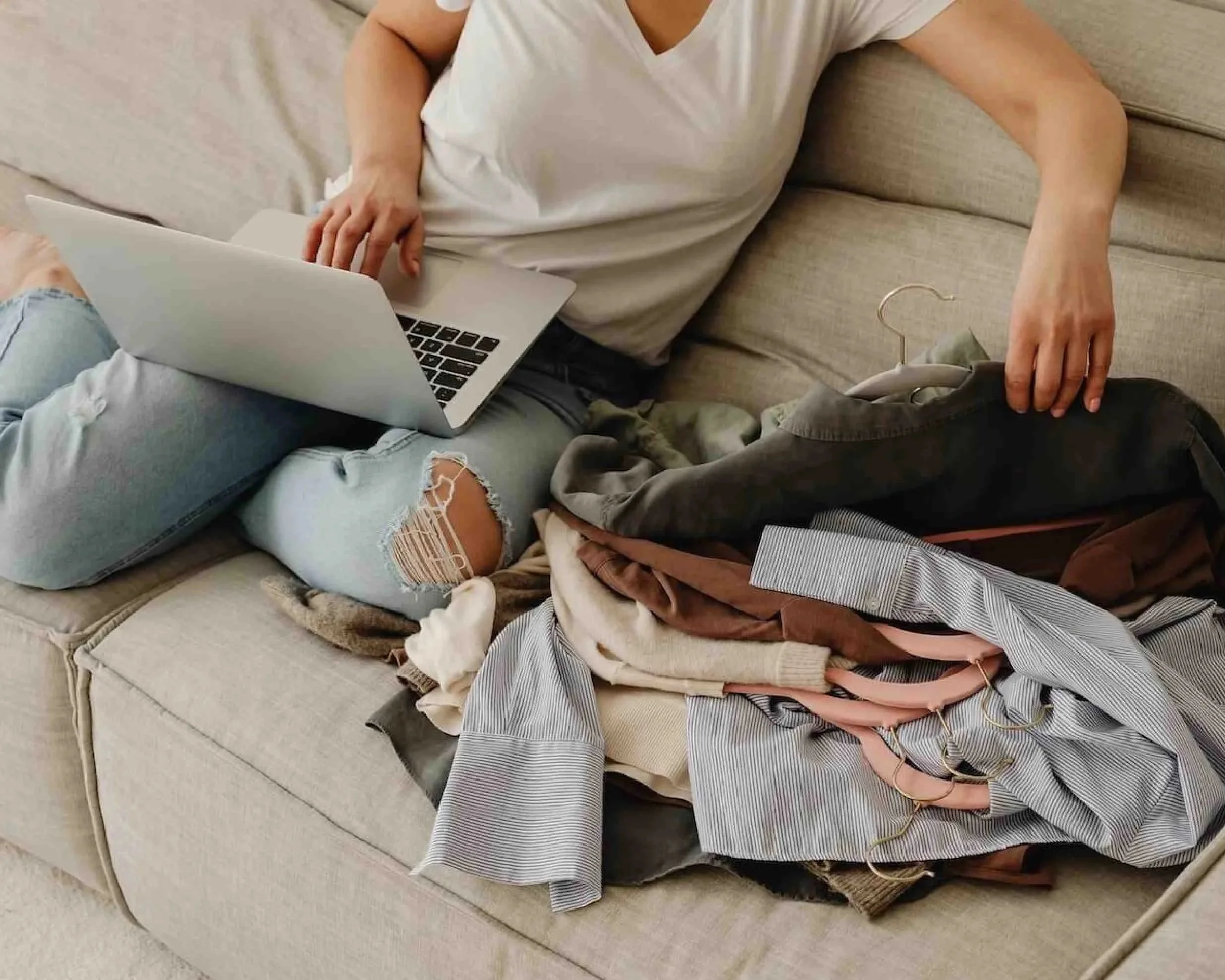Person working through an online decluttering workshop from their sofa, laptop open with a pile of clothes beside them