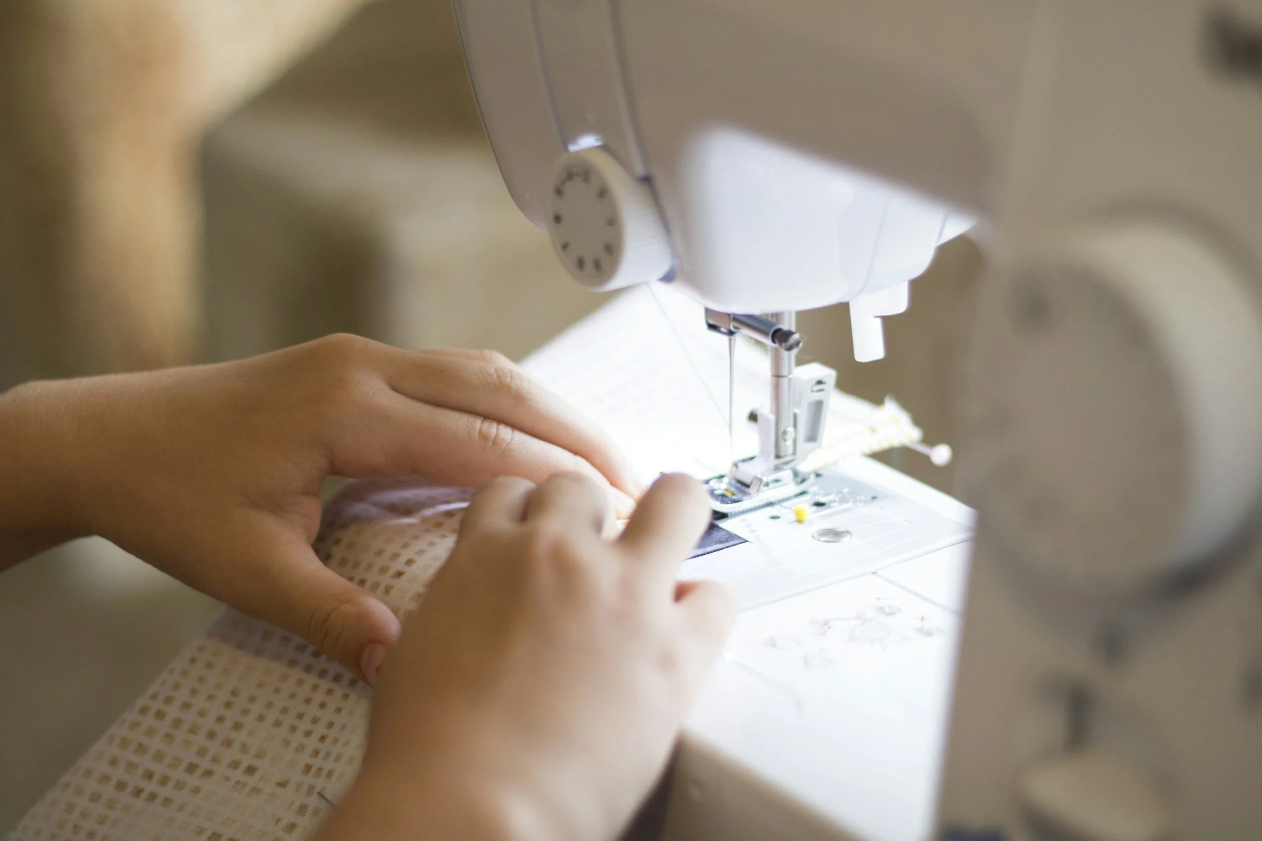 Close-up of sewing machine and hands guiding fabric through it for sewing.