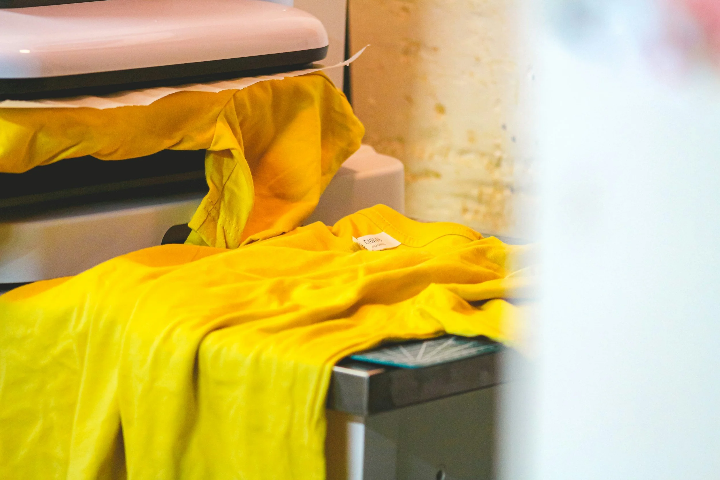 A small appliance, possibly a kitchen scale, on a countertop with a yellow cloth draped over it, partially obscuring a label. There is a yellow fabric item, likely clothing or a textile, in the foreground.