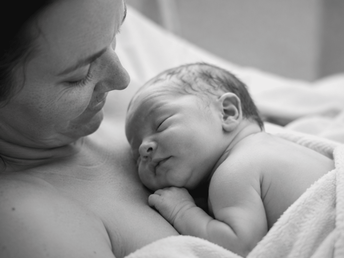 A black and white photo of a mother holding her newborn baby close to her chest, both sleeping peacefully.