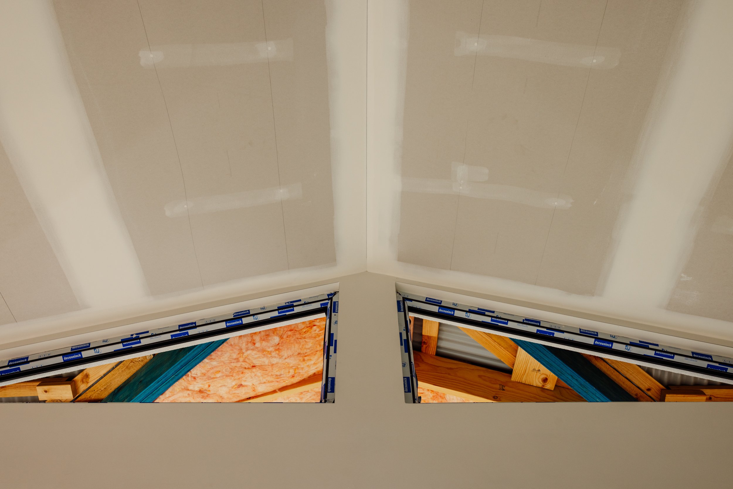Interior view of a porch ceiling with two windows showing wooden beams and construction materials inside.