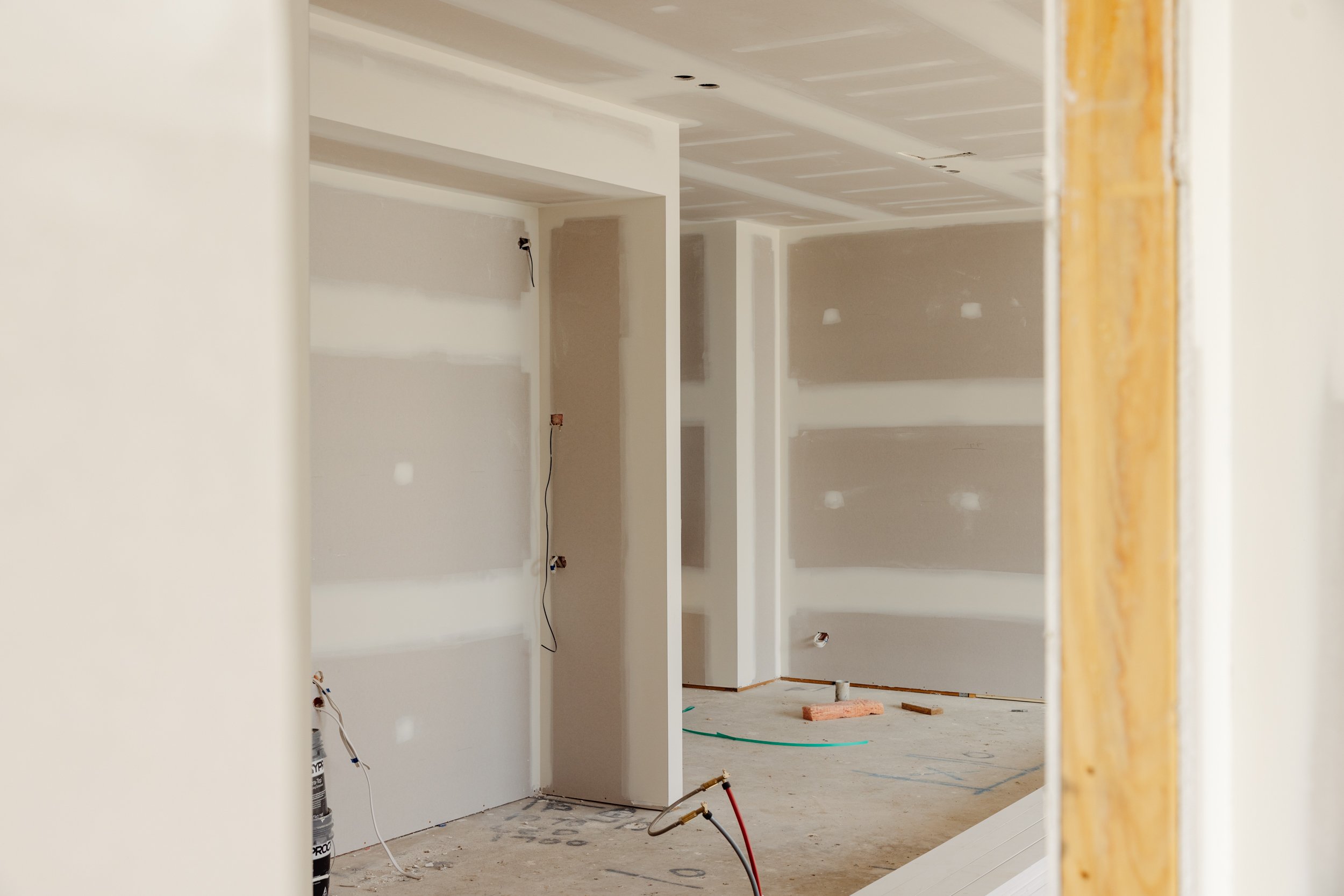 Interior of a house under construction with drywall installed, electrical wiring visible, and unfinished floors.