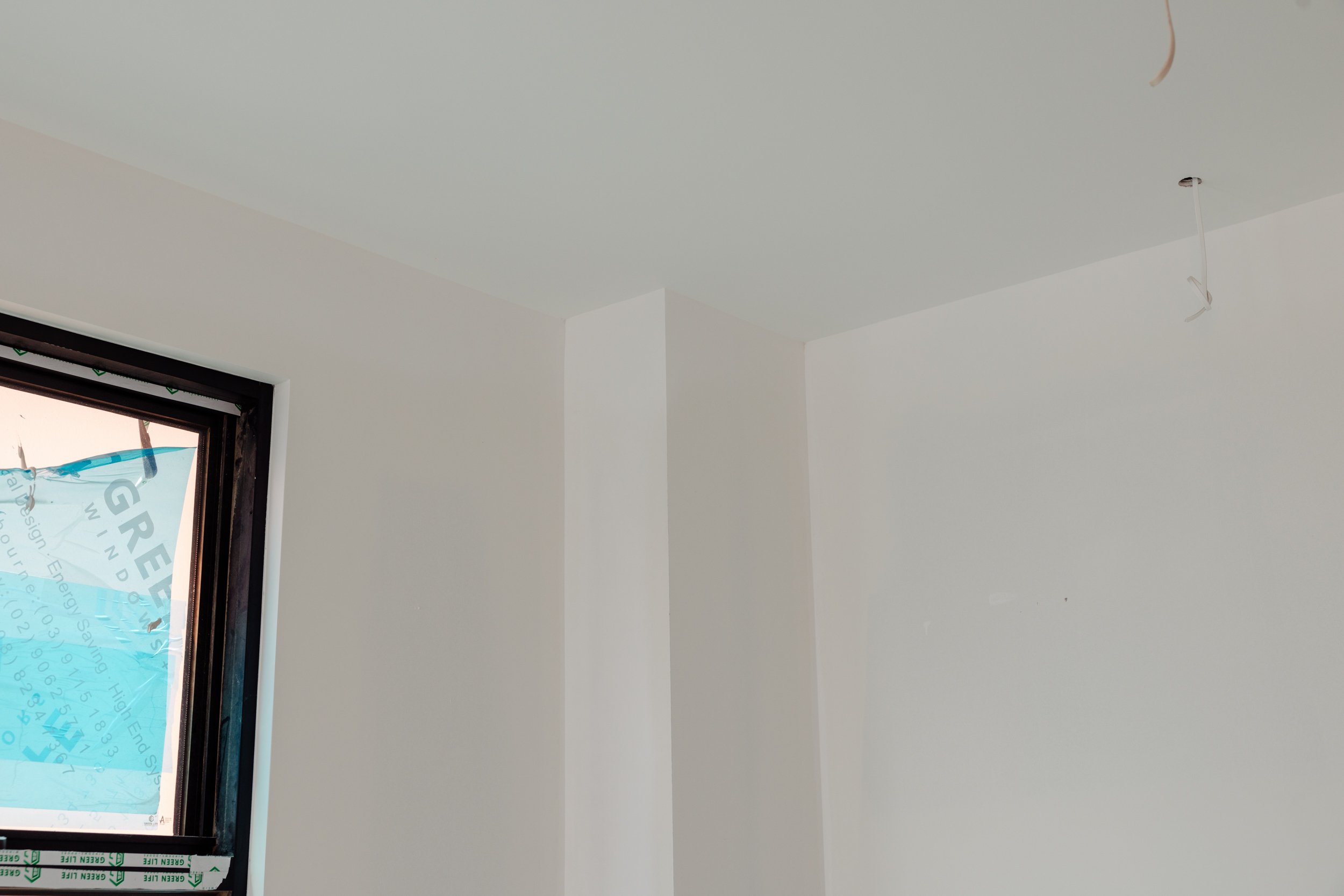 Interior room with white ceiling and walls, a small window in the bottom left corner, and an empty light fixture hanging from the ceiling.