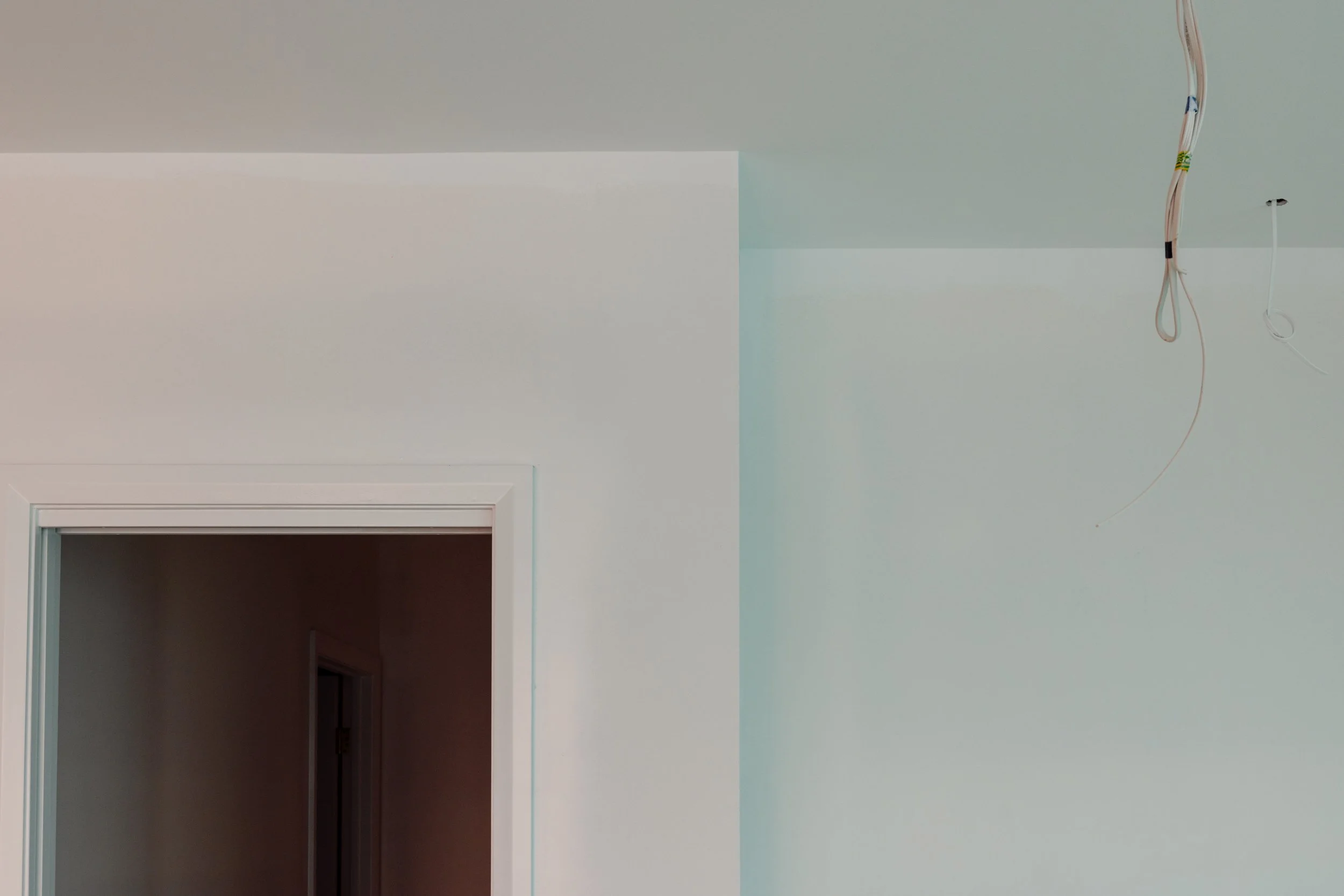 Interior of a room with a doorway and electrical wires hanging from the ceiling.