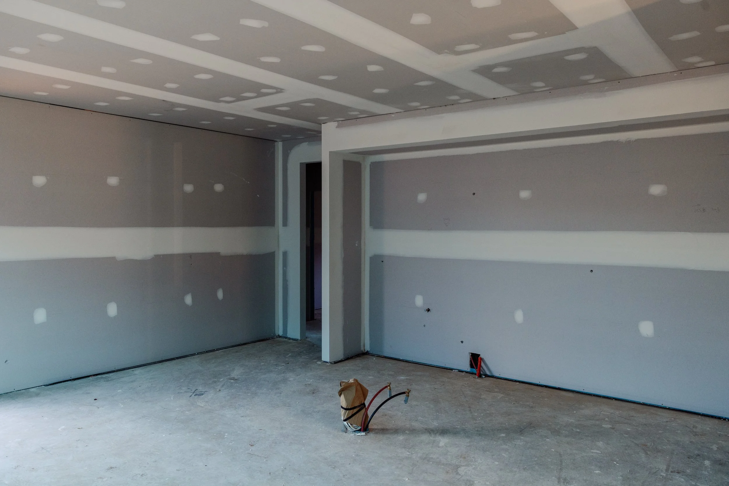 Interior of a room under construction with drywall on the walls and ceiling, with visible electrical wires and outlets, and unfinished flooring.