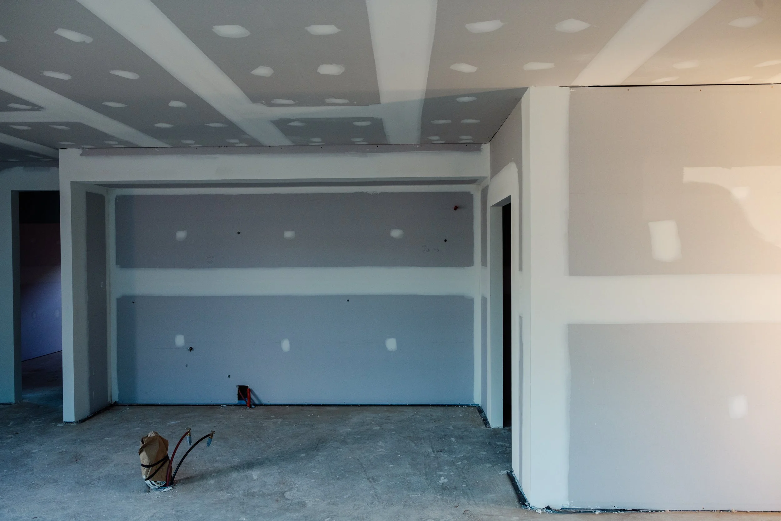 Interior of a room under construction with drywall walls and ceiling, and exposed electrical wiring on the floor.