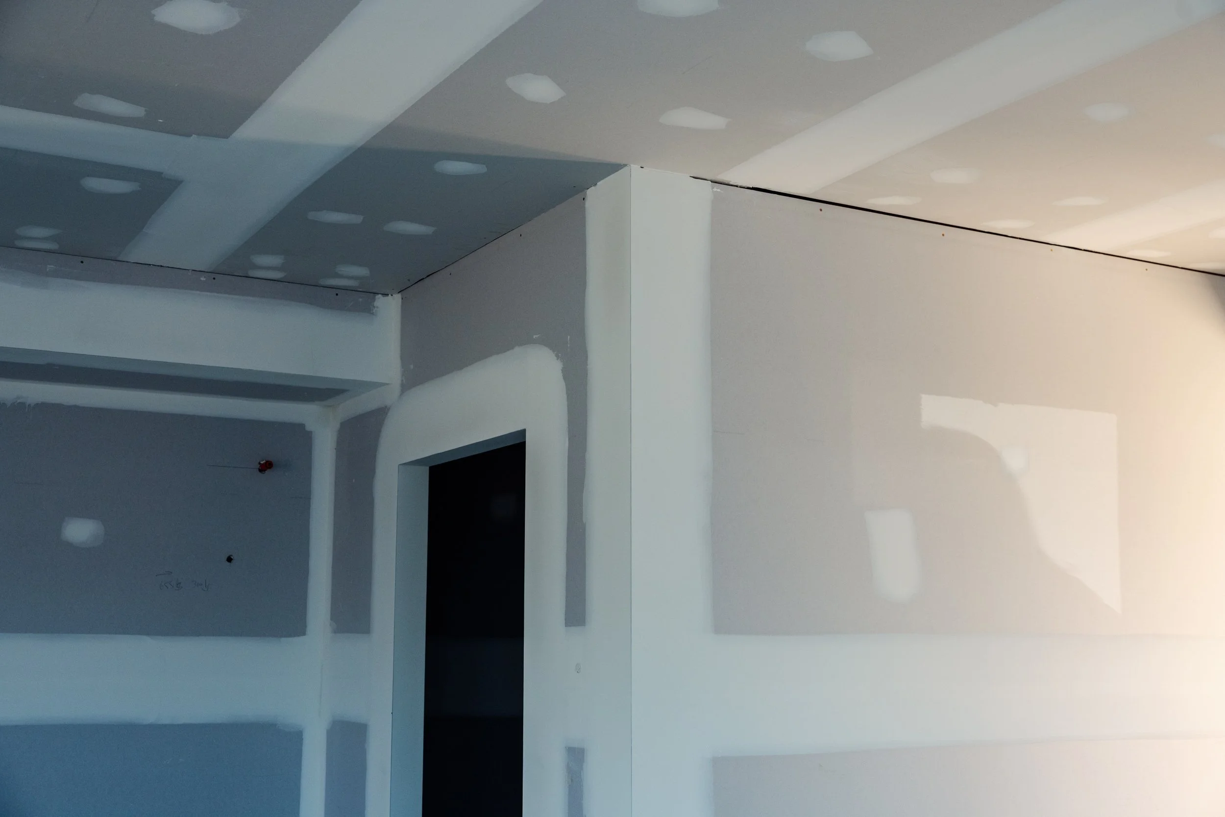 Interior of a room under construction with drywall installation, ceiling drywall in progress, and an open doorway.