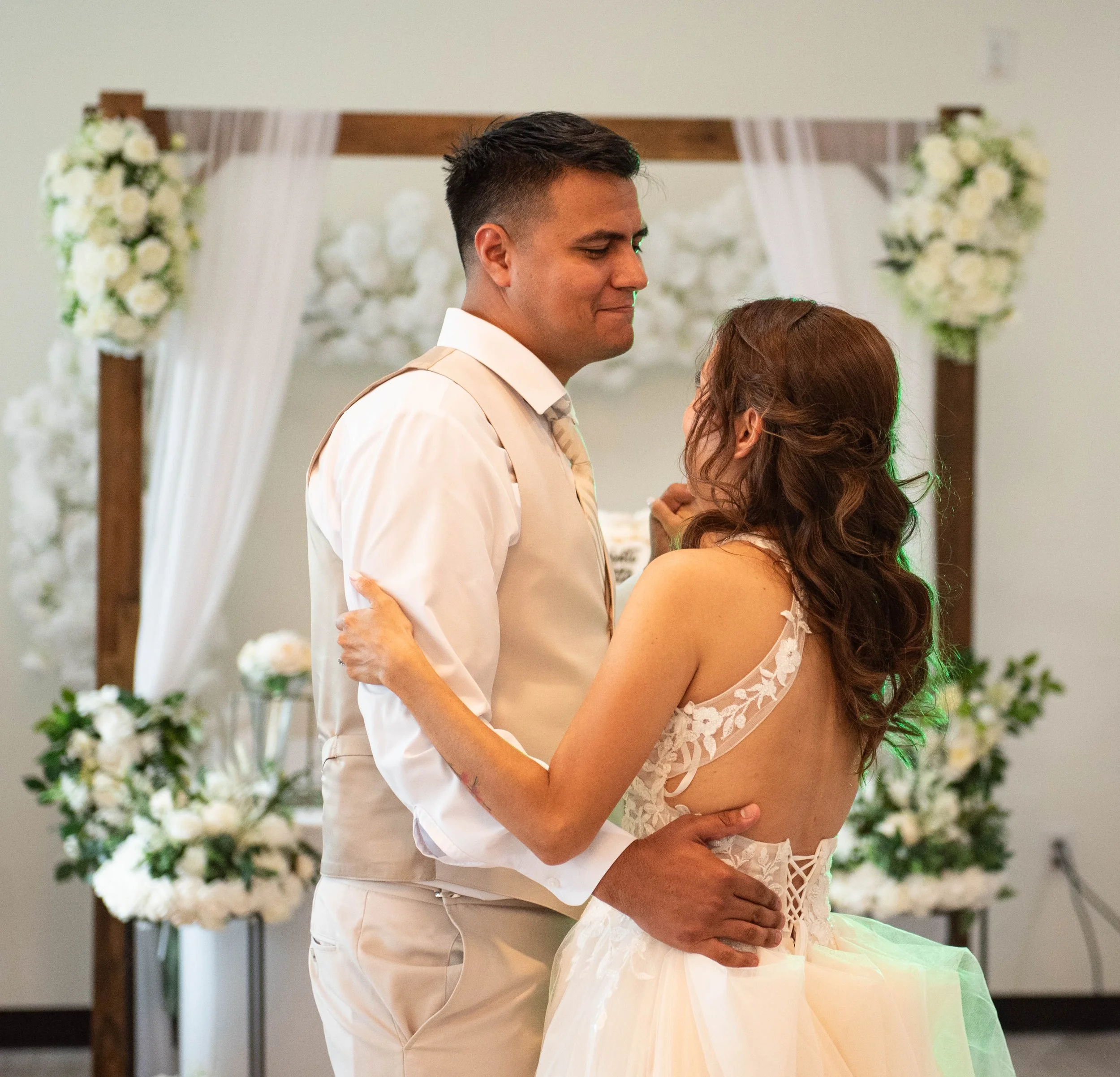 A man and woman share a dance at their wedding, with a floral arch in the background.