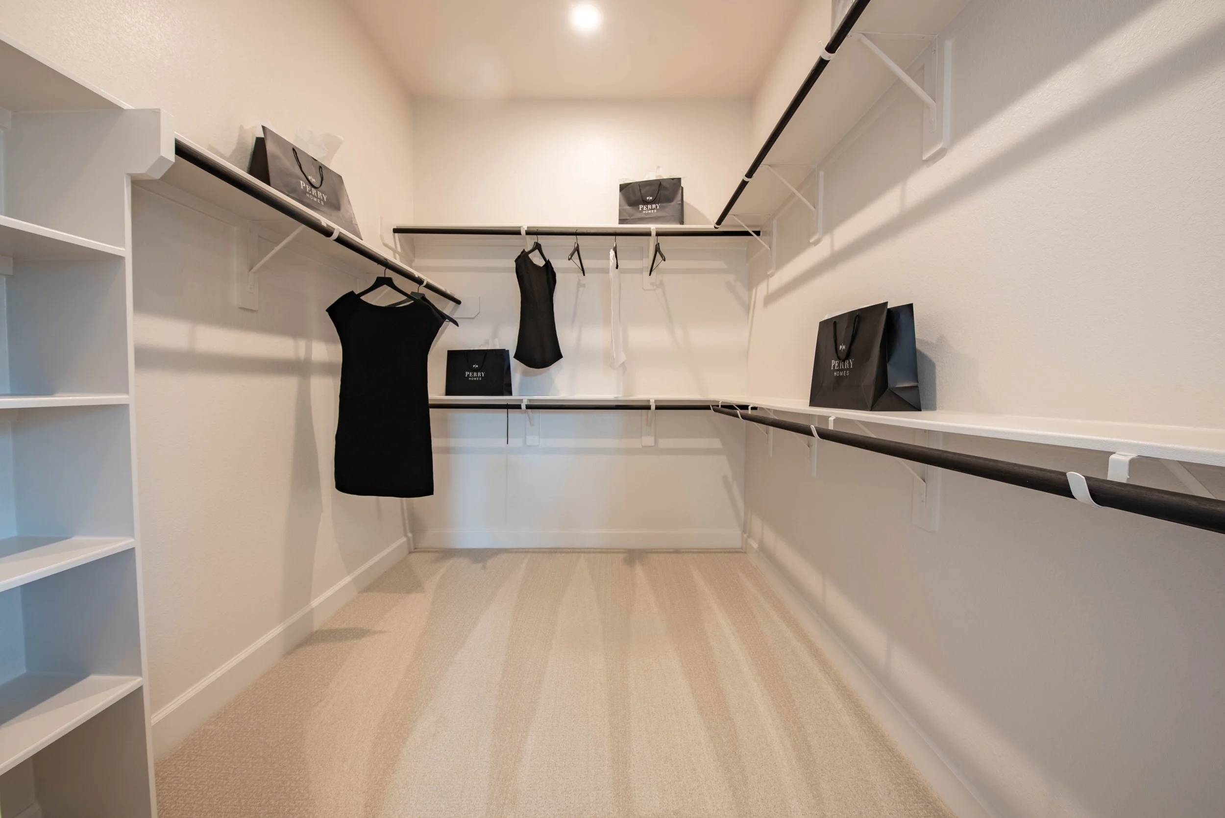 Empty walk-in closet with black hanging bags on shelves, black dresses on hangers, and white shelves on the left side.