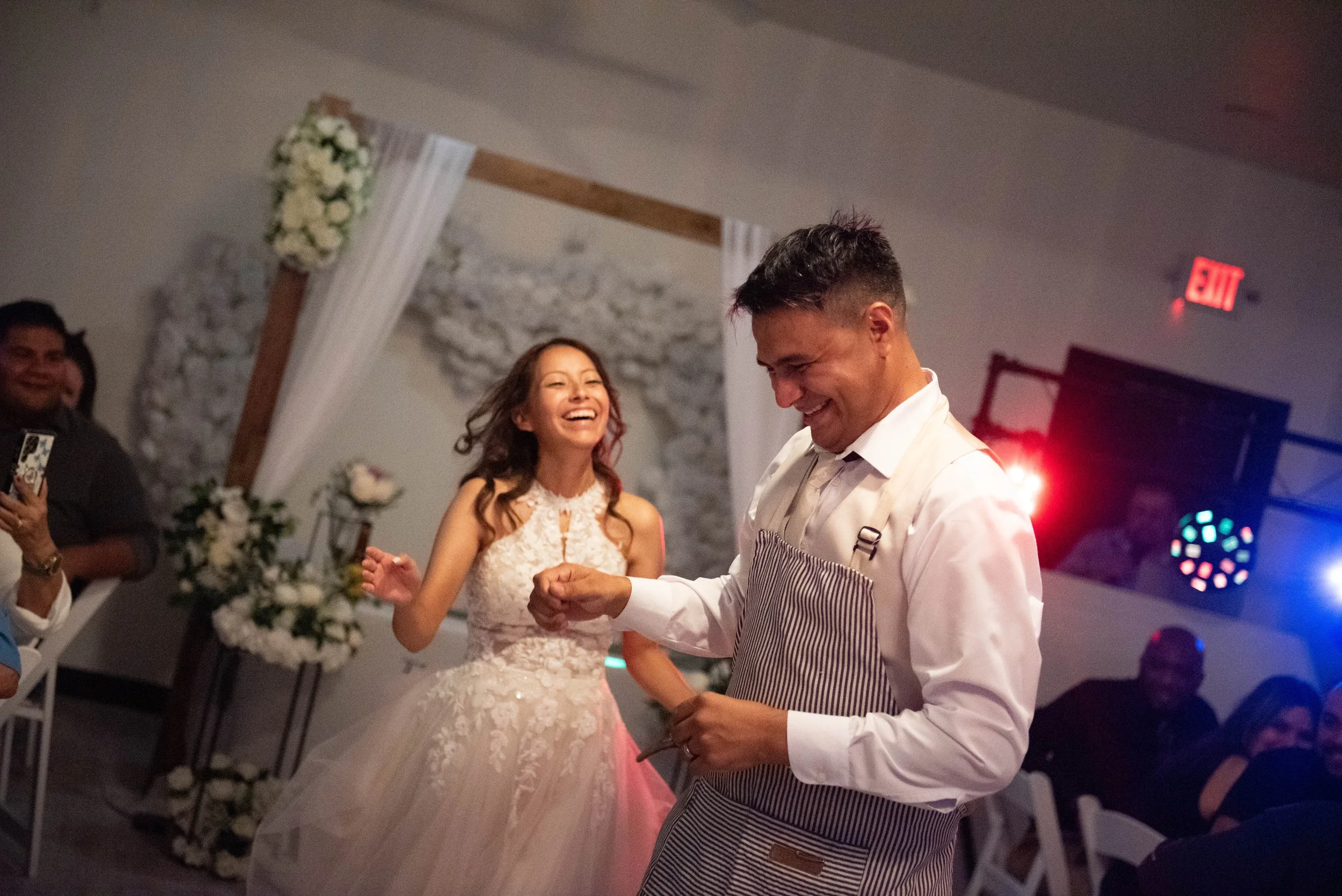 A joyful bride in a lace wedding dress and groom dancing at their wedding reception in a decorated venue.