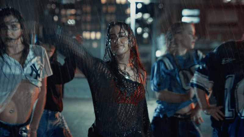 A young woman dancing in the rain with other people around her on a city street at night. Music Video, Pop music video, Melbourne-based pop music artist Aanya. Melbourne music video, dance pop, dancing on top of a carpark in the rain. Step-up.