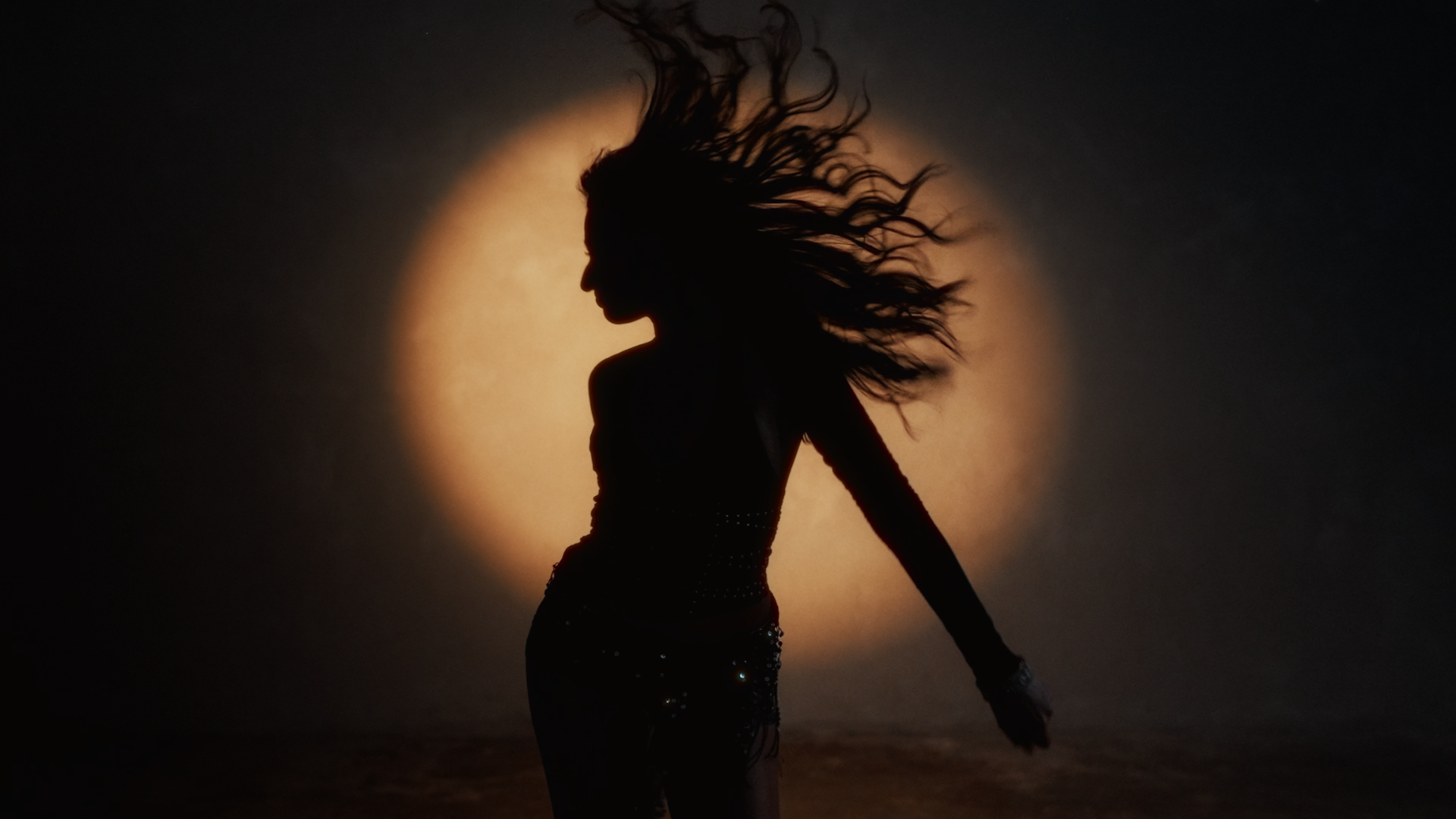 Silhouette of a woman with long hair flowing in the wind, standing against a large backlit moon. Music Video, Pop music video, Melbourne-based pop music artist Aanya. Melbourne music video, dance pop, Player music video.