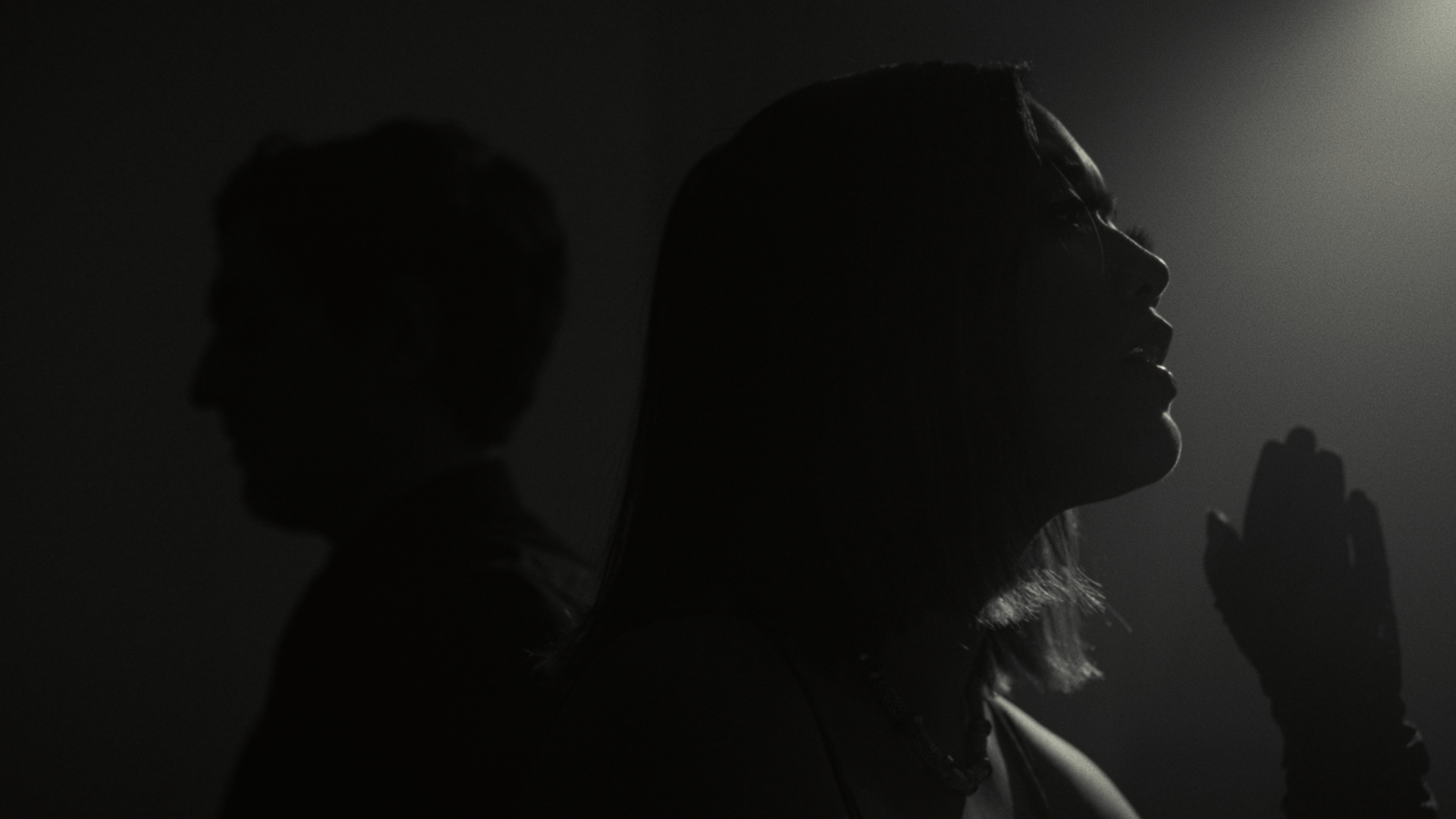 Silhouette of a woman with eyes closed and a serene expression, with hand raised in prayer or focus, illuminated by soft light from the side.