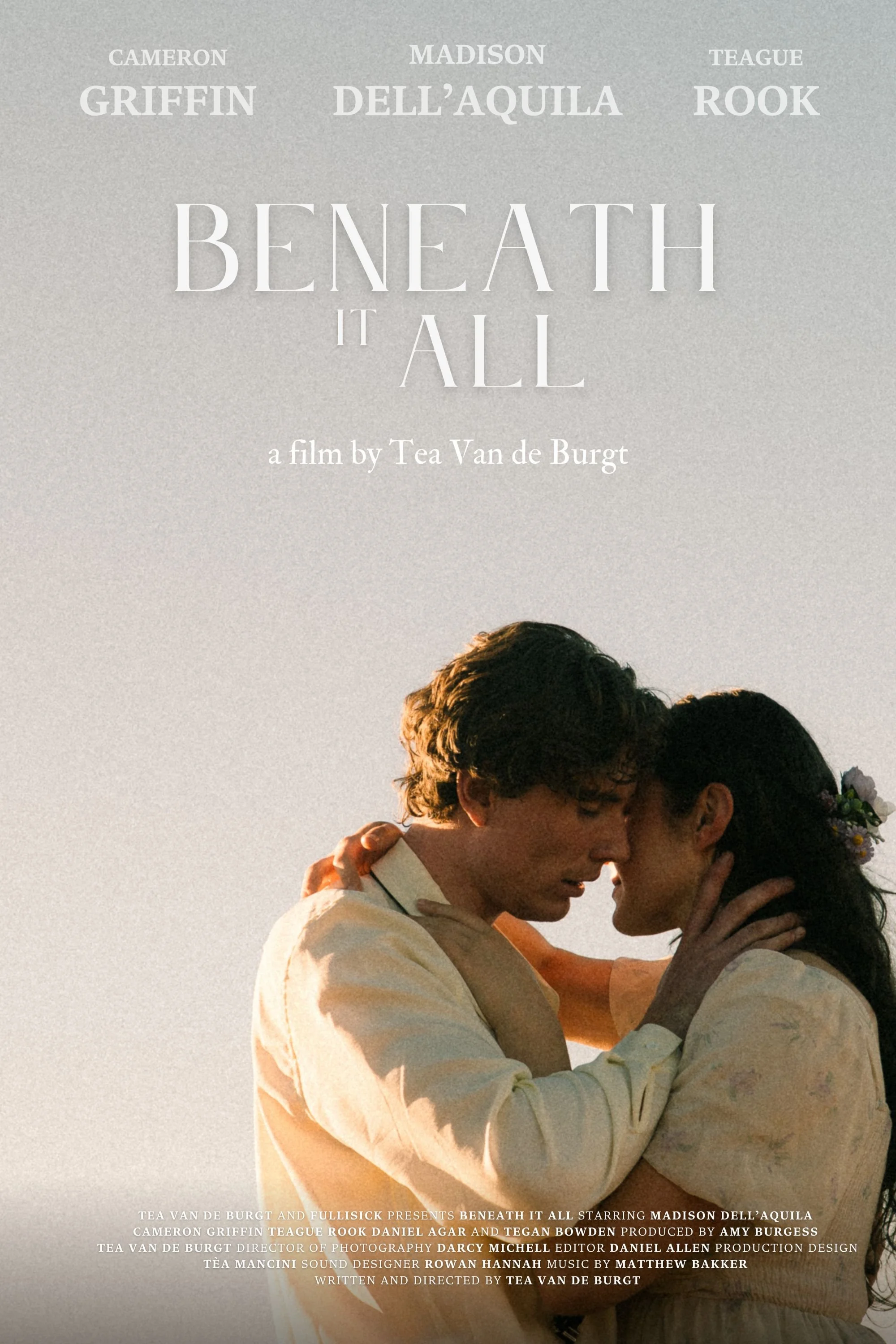 A close-up photo of two people embracing each other, with one person touching the other's face, during sunset. The photo is part of a promotional poster for the film "Beneath It All" directed by Tea Van de Burg.