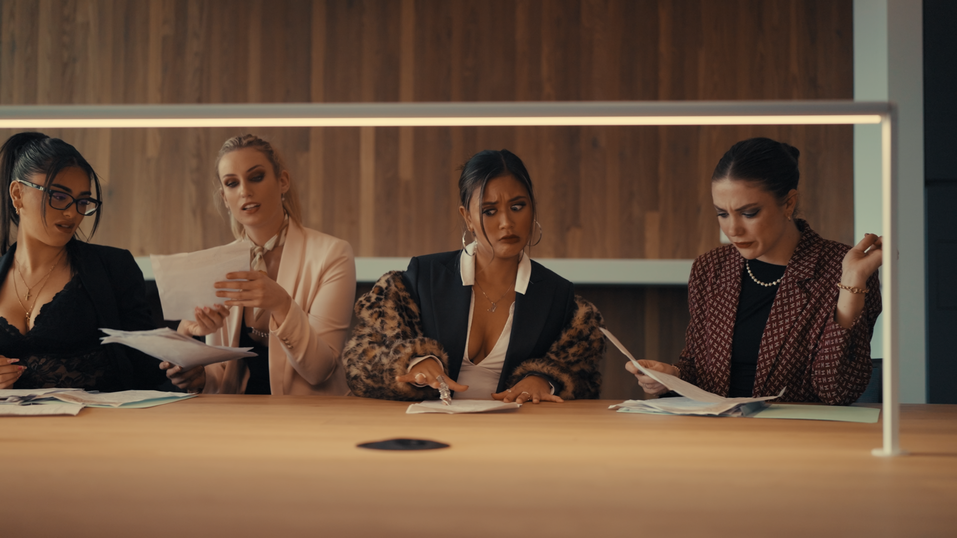 Four women sitting at a table with papers, appearing frustrated or concerned at a business meeting.