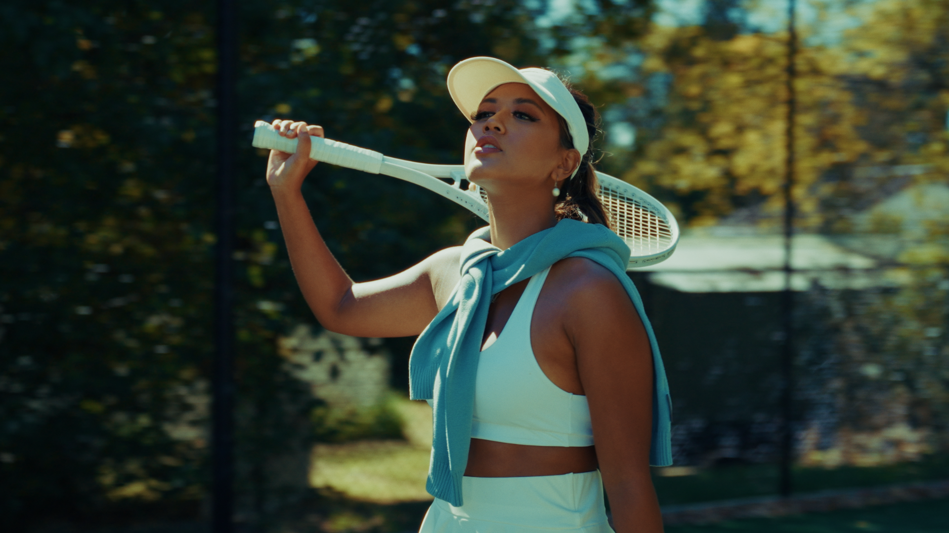 A woman in tennis attire carrying a tennis racket over her shoulder outdoors on a sunny day. Challengers-themed. Directed by Tea Van de Burgt.
