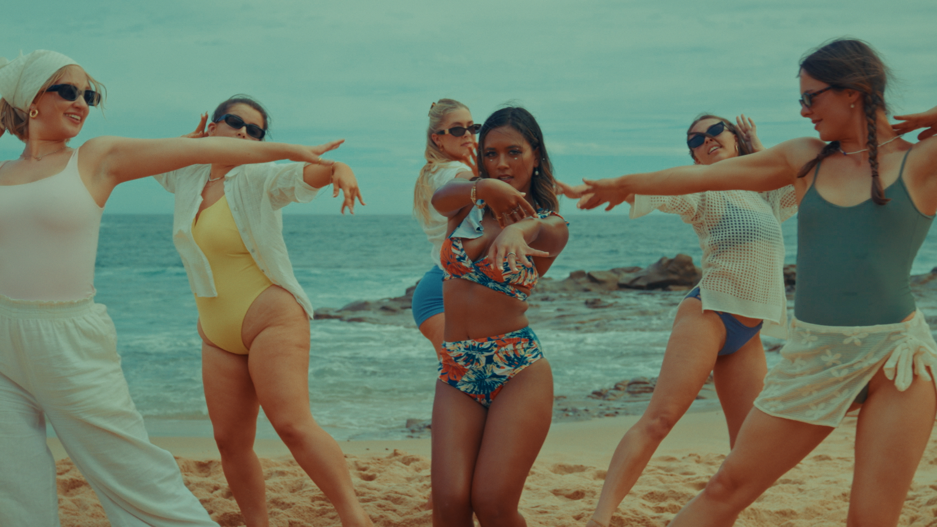 Group of women dancing on the beach, wearing swimsuits and sunglasses. Alisya Rae 'Show Me' Music Video Melbourne. Directed by Tea Van de Burgt.
