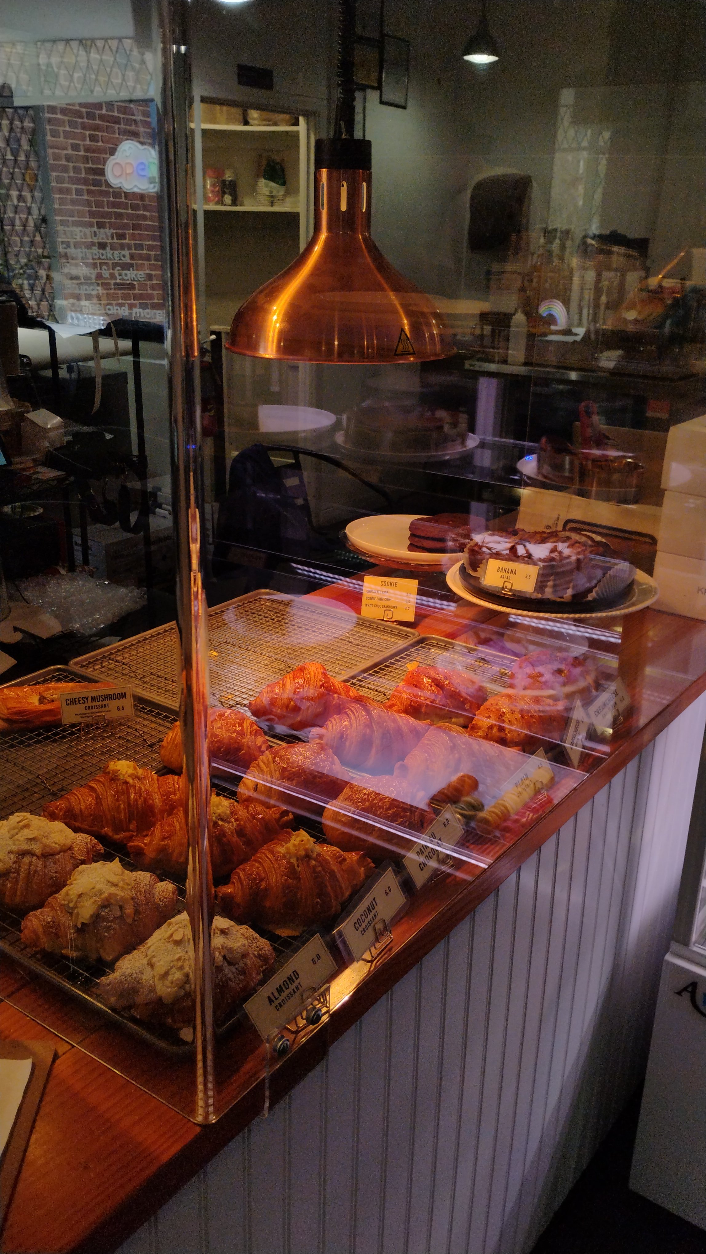 Pastry display case with croissants, muffins, and other baked goods in a bakery storefront.