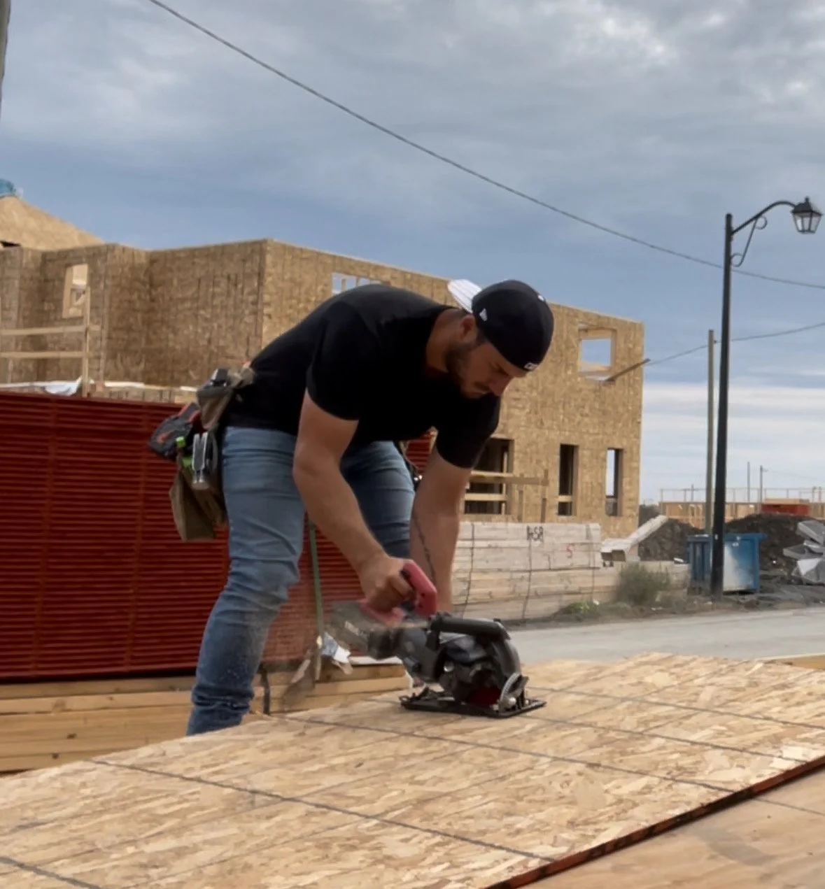 A man at a construction site cutting wooden boards with a power saw.
