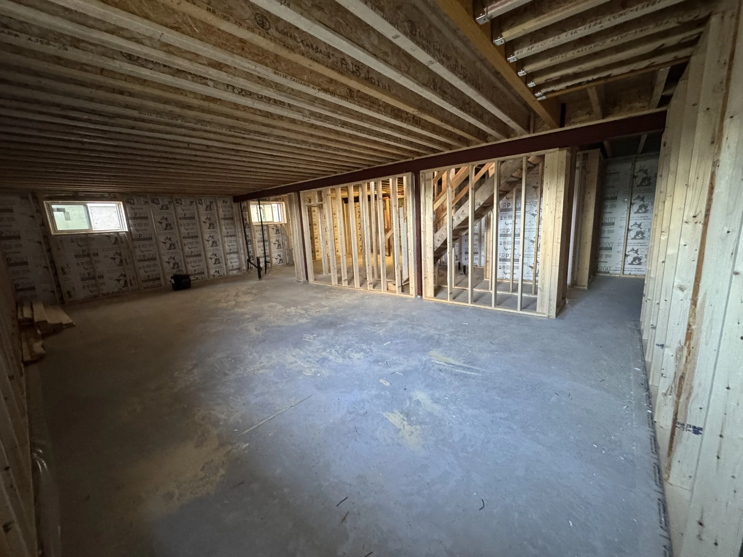 Interior of a house under construction with exposed wooden framing, stairs, and small windows.