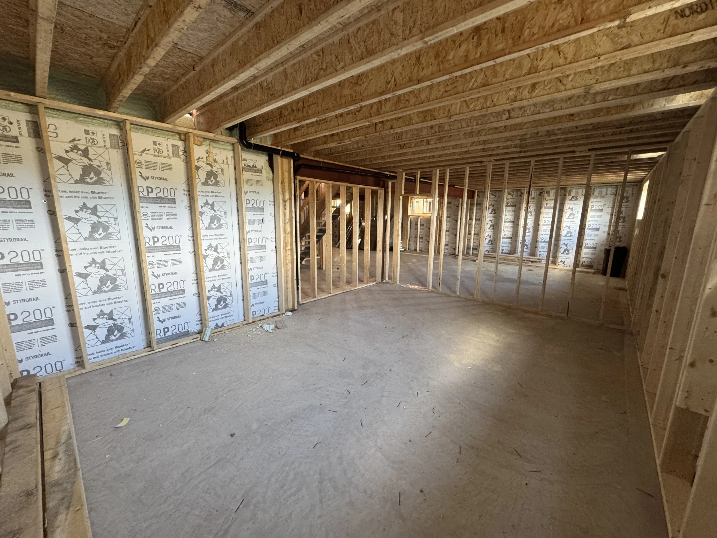 Interior view of a building under construction showing unfinished wooden framing and insulation panels on the walls.
