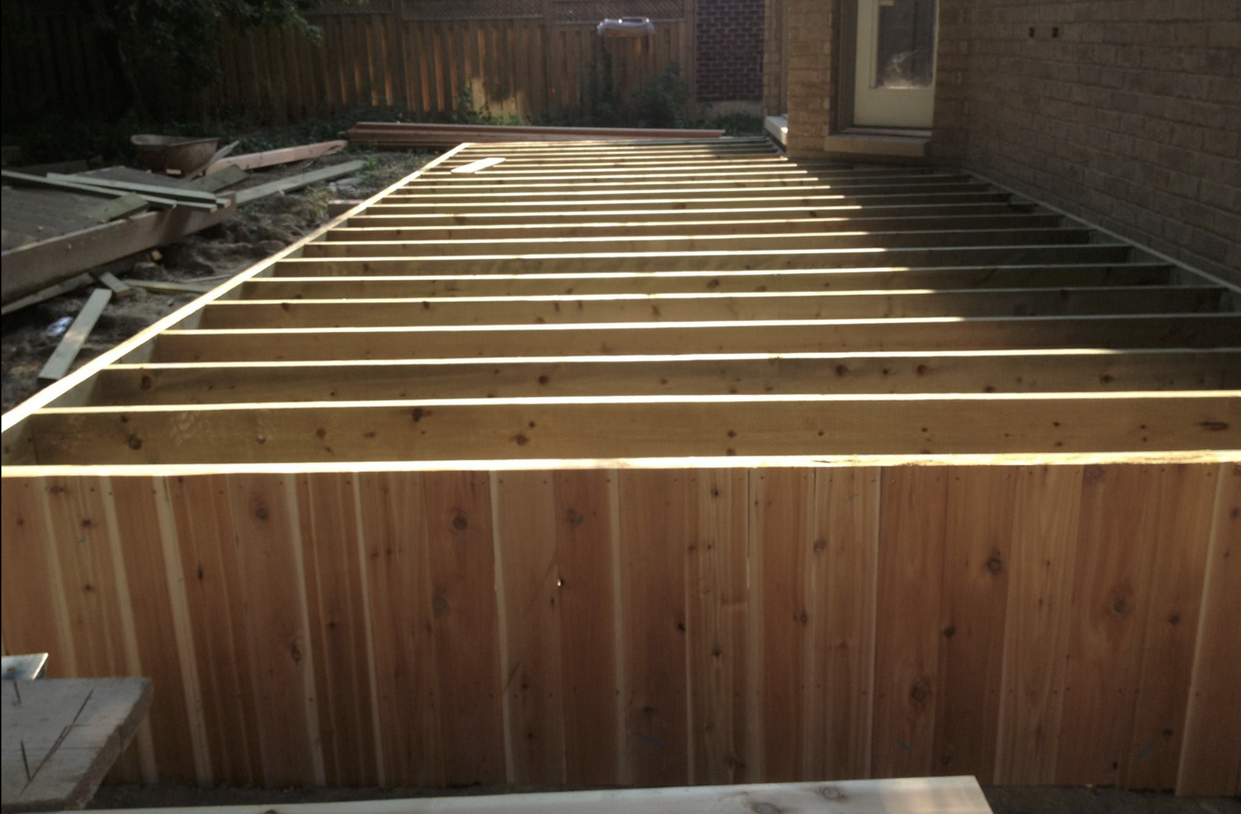 Wooden deck with framing for a new construction or renovation, attached to a brick house, during daylight.