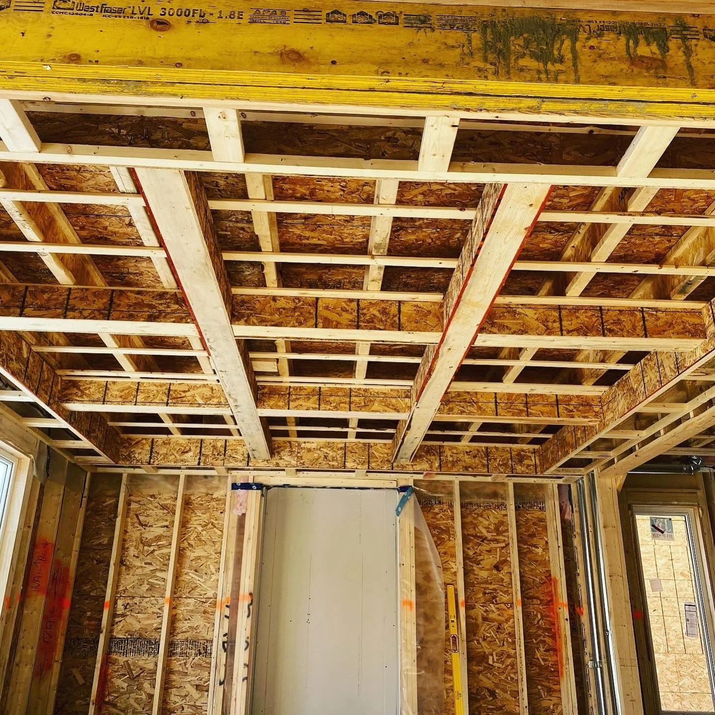 Construction framing of a room in a building under construction with wooden studs, wall sheathing, and ceiling joists visible.