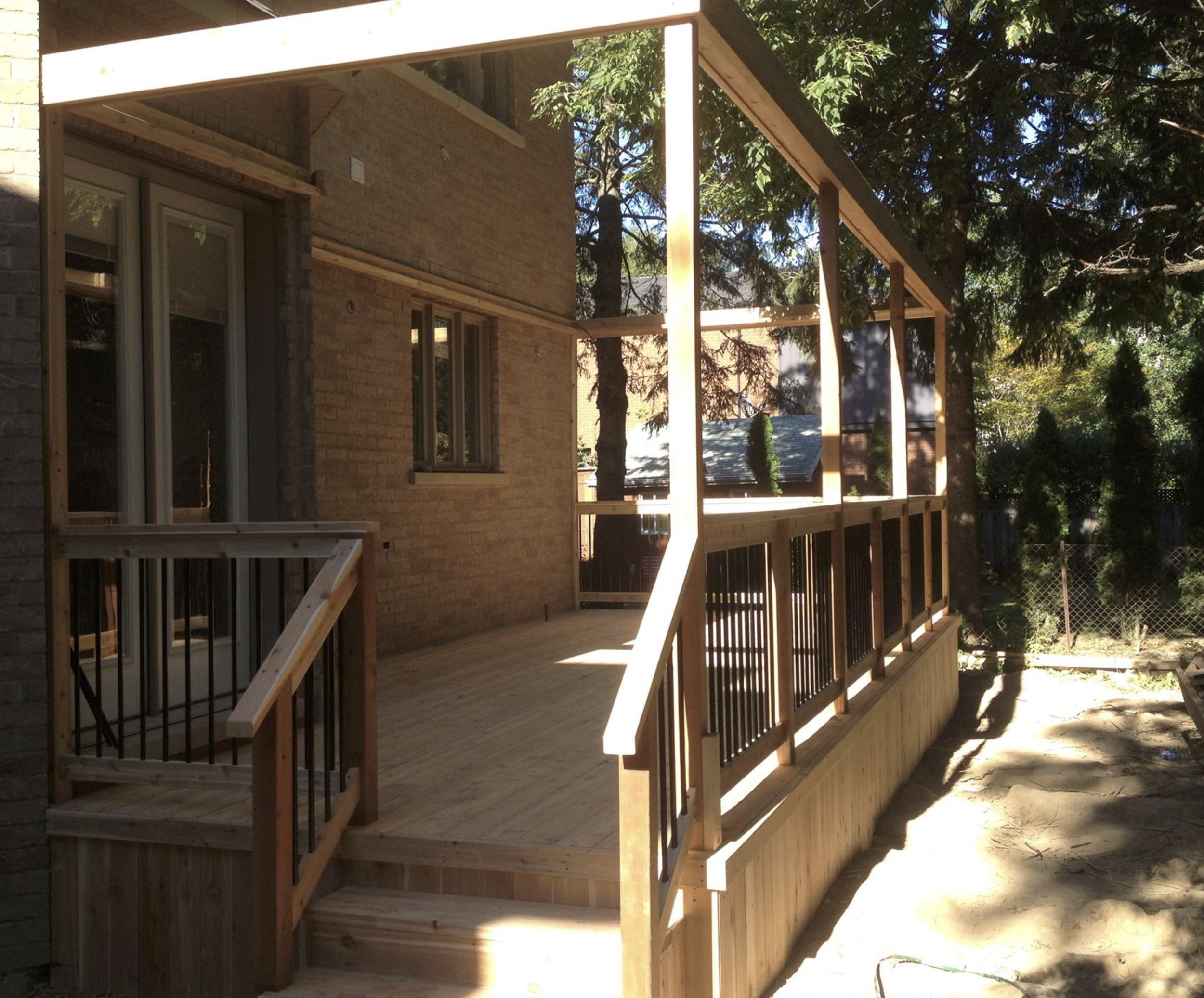 A wooden deck under construction attached to a brick house, with trees surrounding it.