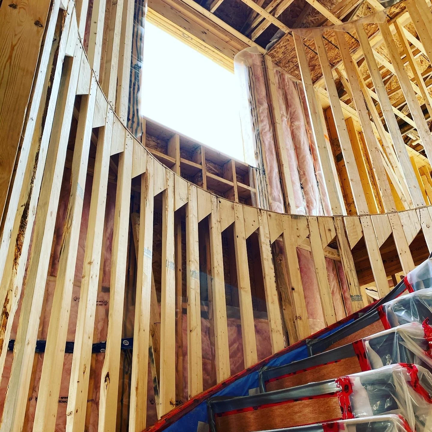 Interior view of a building under construction showing exposed wooden framing, insulation, and a large window opening.