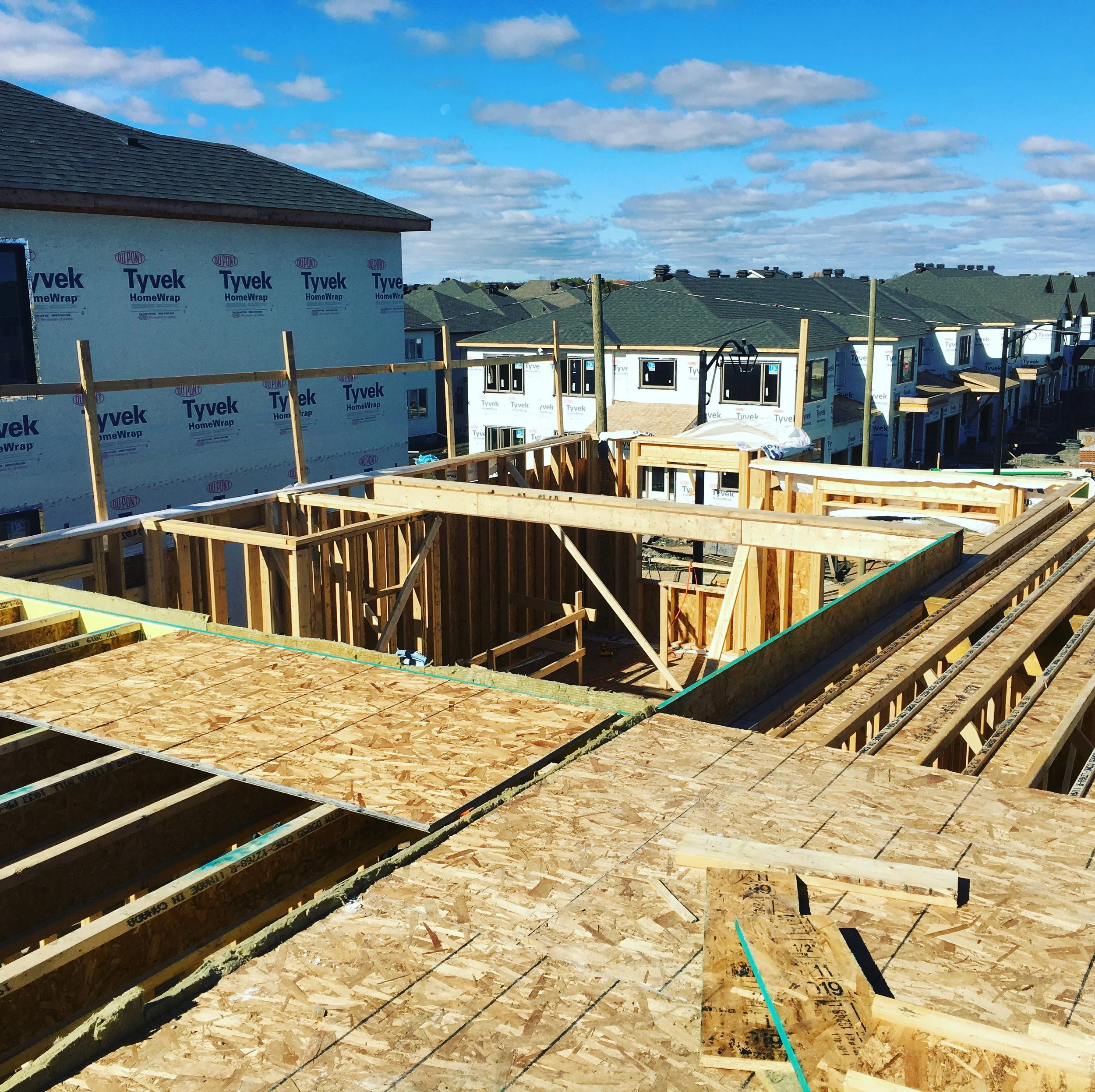 Construction site with framing and roofing in progress on multiple houses, blue sky with clouds overhead.
