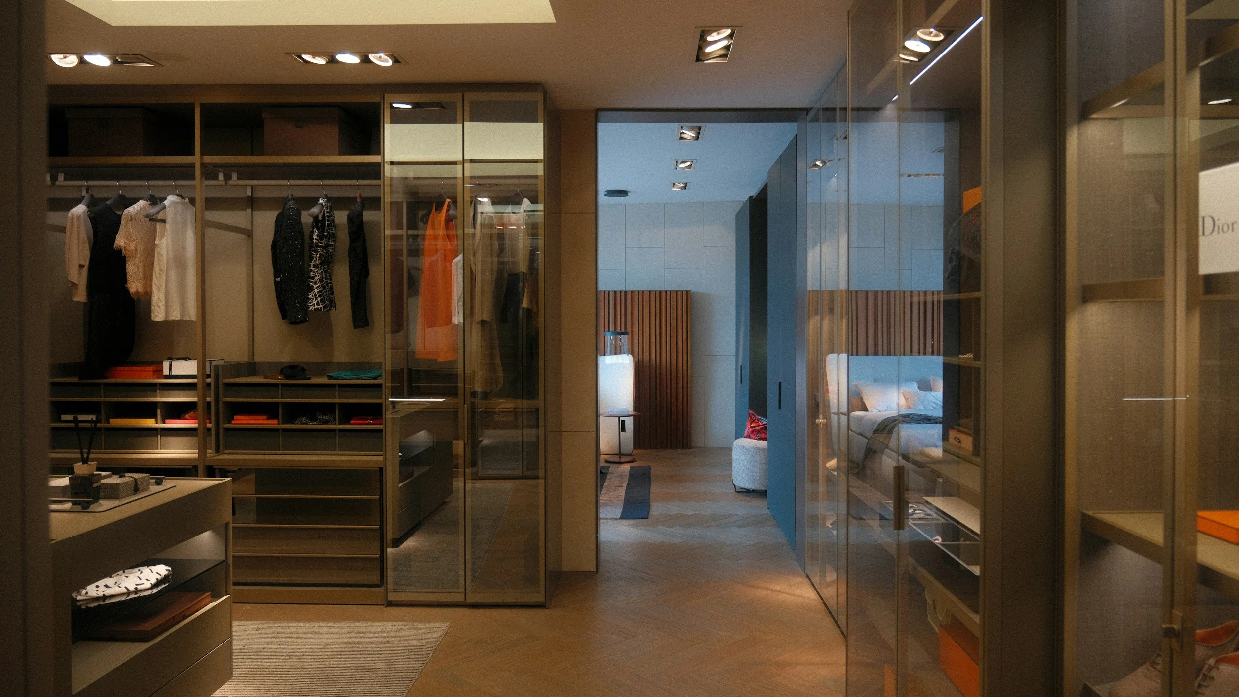 Interior view of a boutique or clothing store with clothing on display, glass shelves, and a glimpse into a cozy living space with a sofa and decorative lamp.